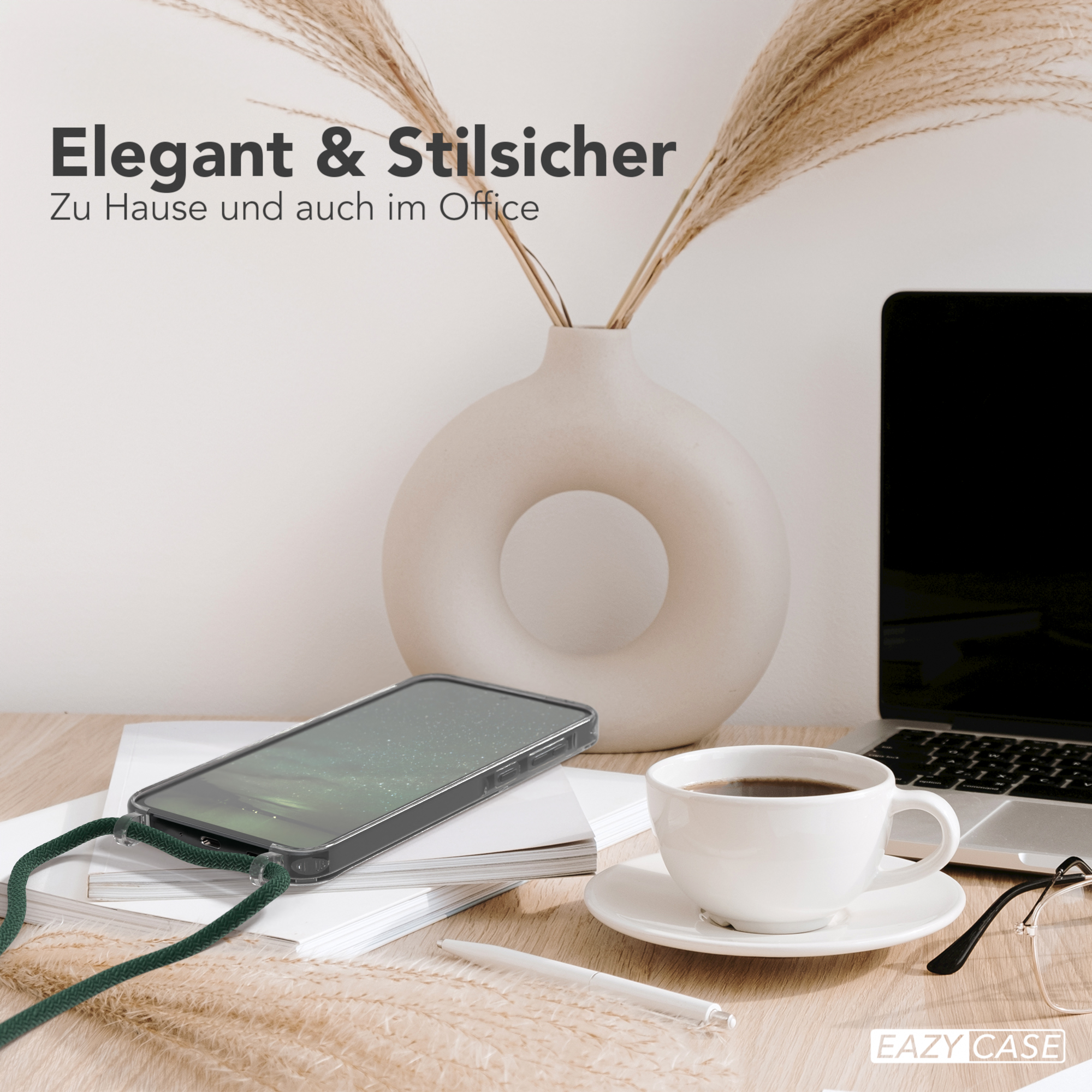 Ein Telefon mit grünem Riemen, ein Laptop und eine Kaffeetasse auf einem Schreibtisch mit Vase und Brille.