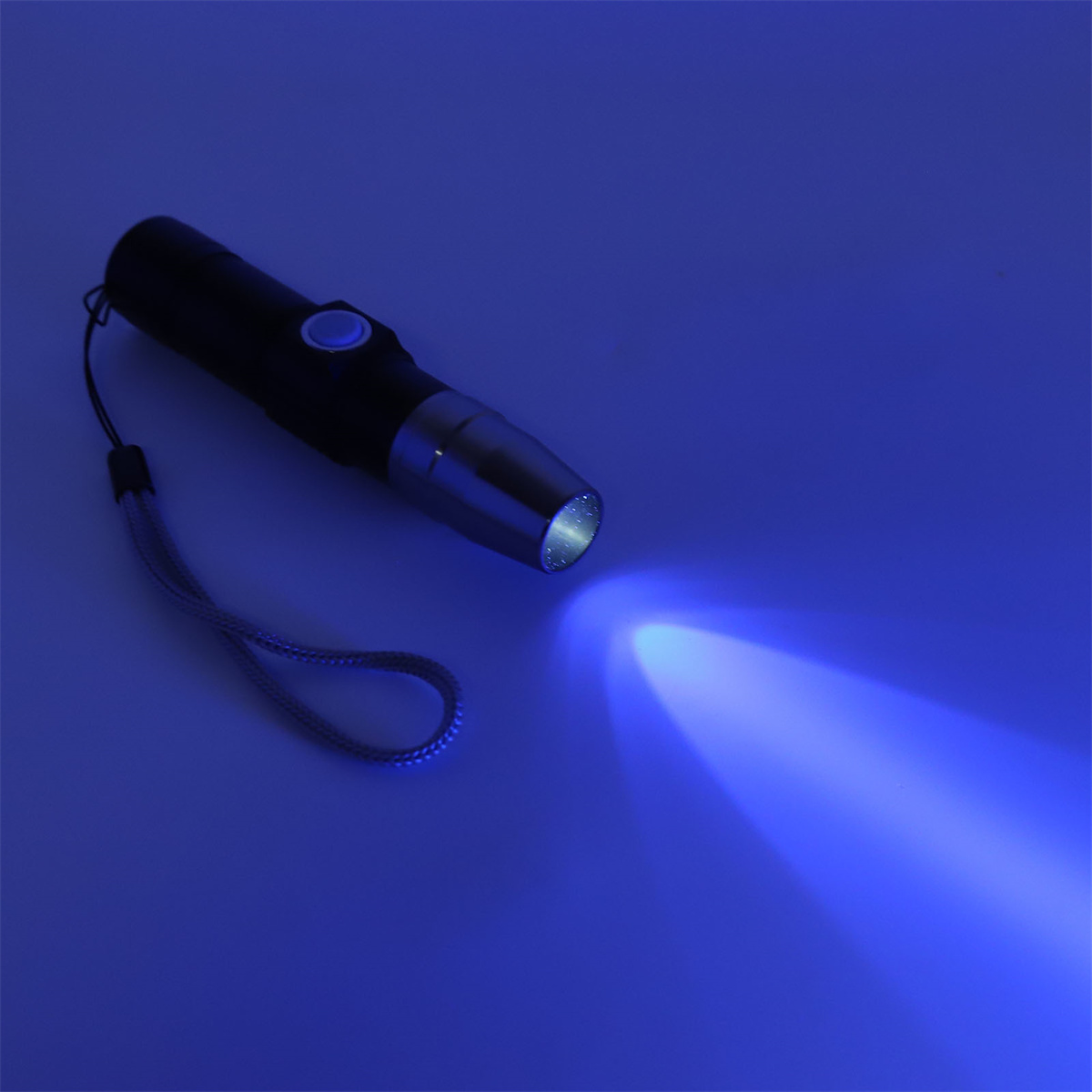 Schwarze Taschenlampe, die einen blauen Lichtstrahl aussendet. Die Taschenlampe liegt auf blauer Fläche.