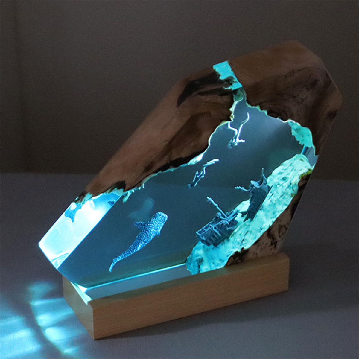 Eine Holzskulptur mit blau leuchtendem Inneren, die einen Wal und Taucher zeigt.