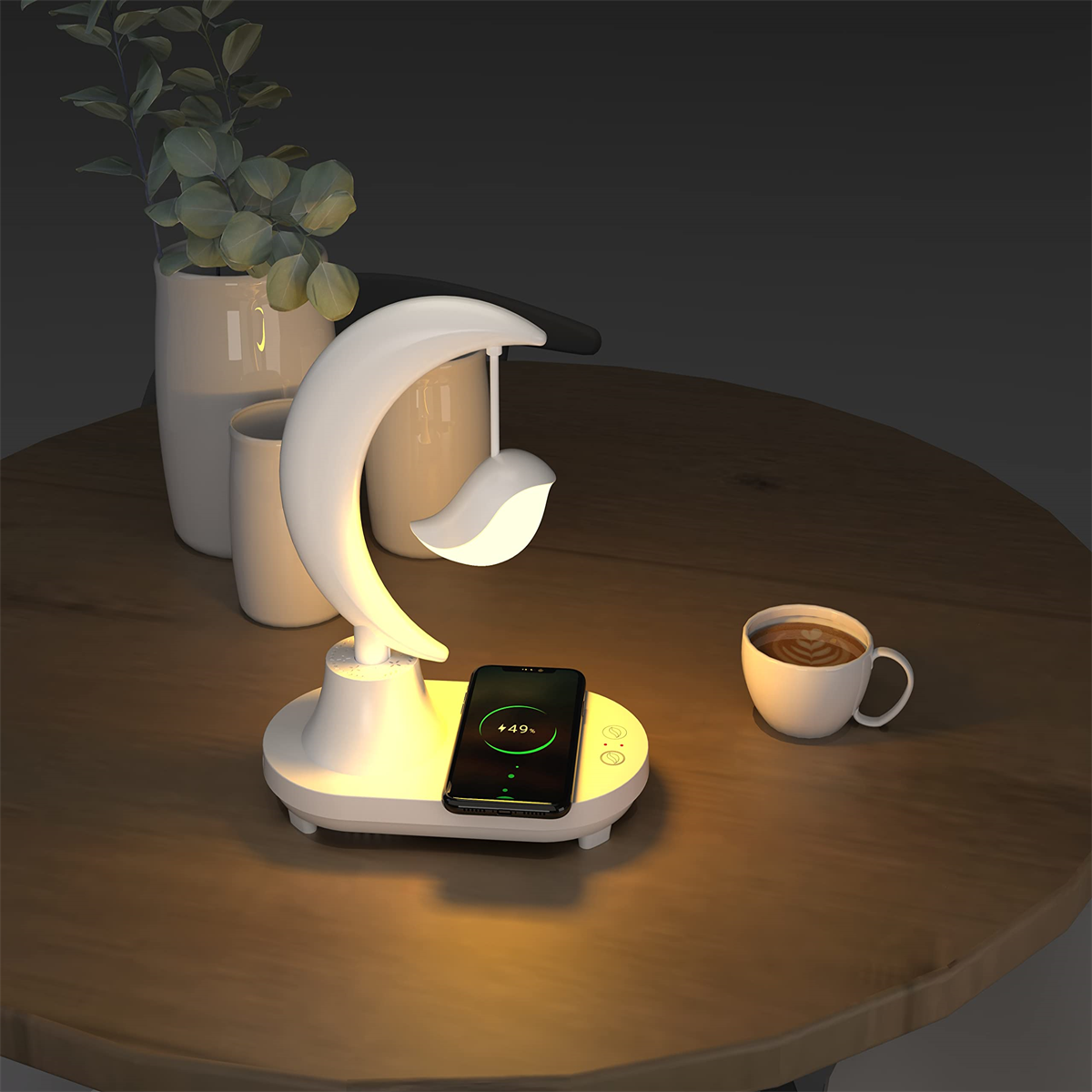 Weiße Lampe mit Monddesign. Ein Telefon wird auf der Basis geladen, mit einer Kaffeetasse.