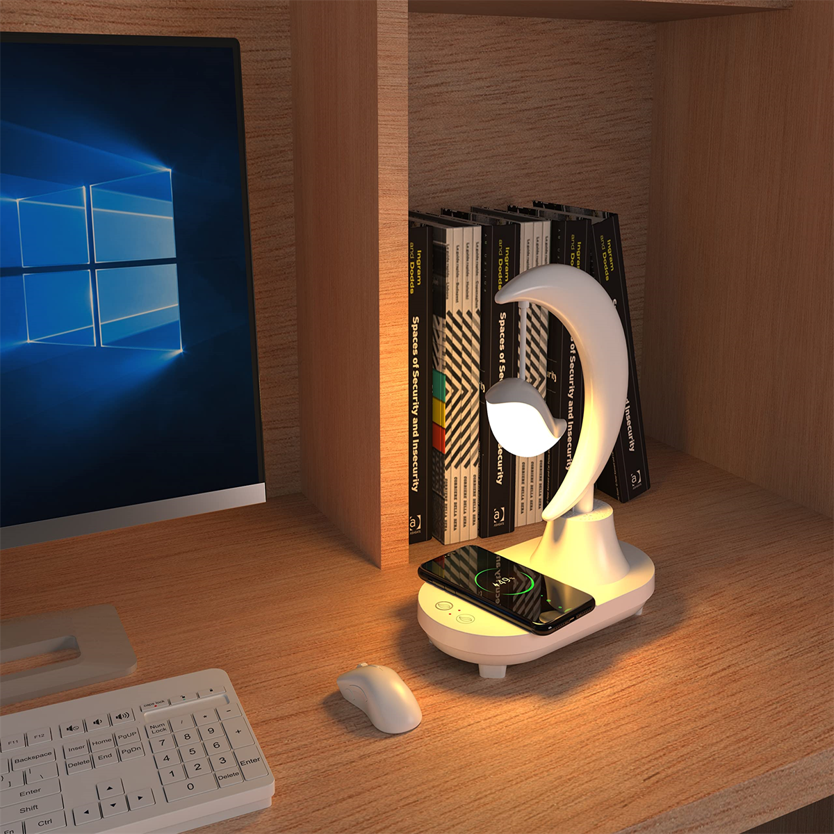 Schreibtisch mit Lampe, Telefon lädt. Bücher, Computer und Maus sichtbar. Holzregale.