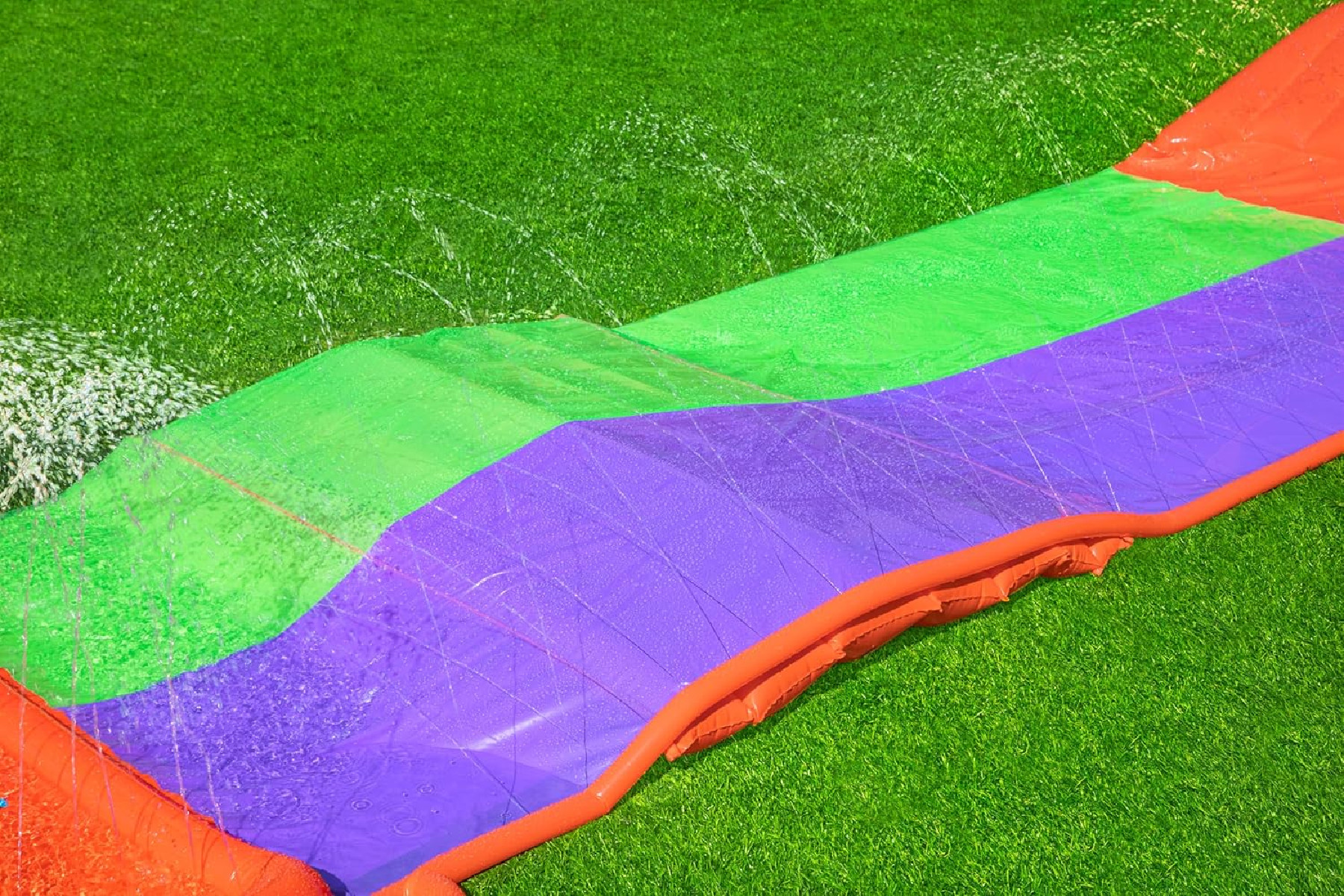 Eine bunte Wasserrutsche auf grünem Gras, Wasser spritzt herunter.