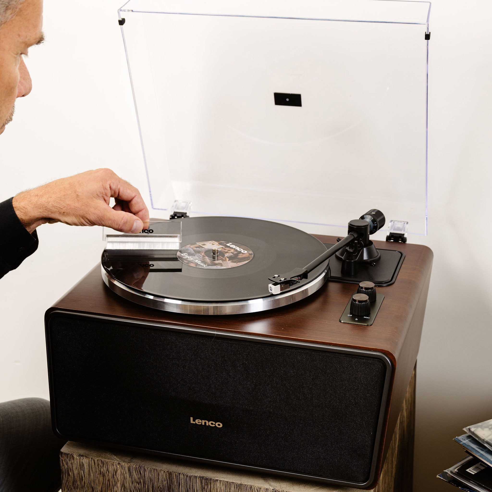 Mężczyzna trzyma płytę. Gramofon z grającą płytą. Brązowa drewniana szafka z głośnikiem.