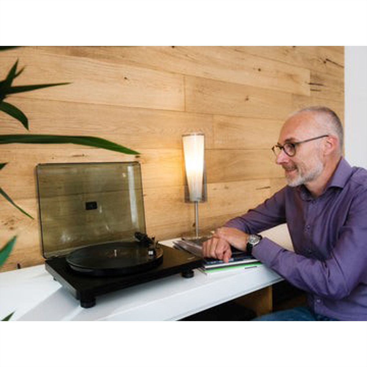 Mężczyzna słucha gramofonu, z lampą i drewnianą ścianą w tle.