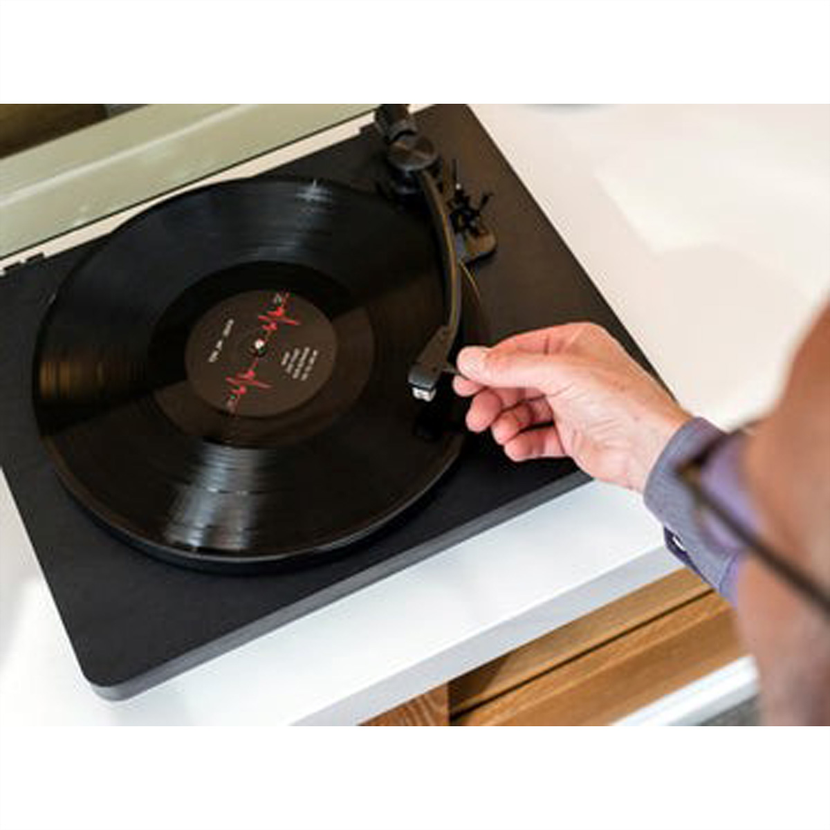 Gramofon z czarną płytą winylową na wierzchu, z ręką, która ma jej dotknąć.