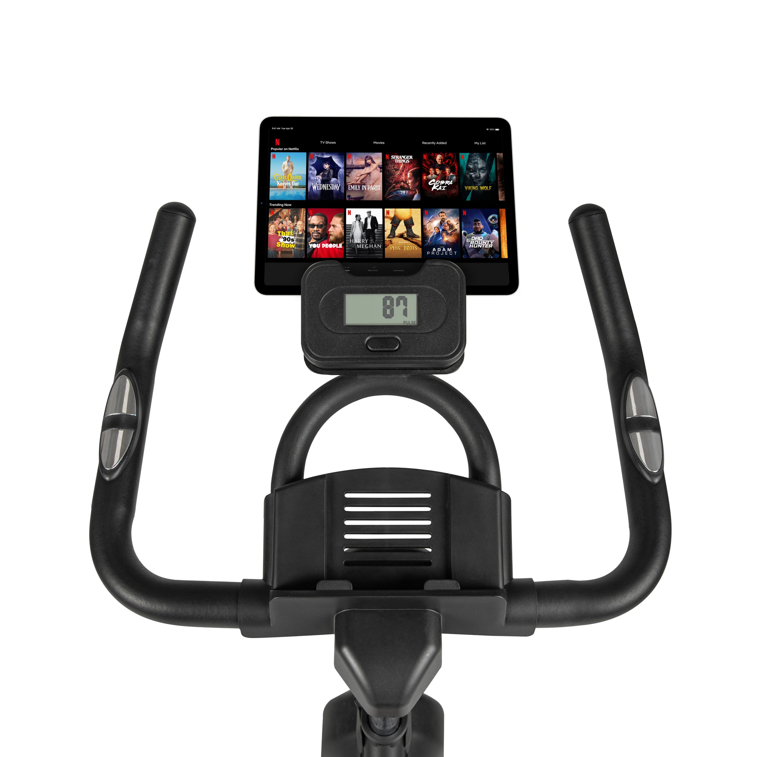 Ein stationäres Fahrrad mit einem Tablet, das einen Streaming-Dienst zeigt. Der Lenker hat Bedienelemente. Weißer Hintergrund.