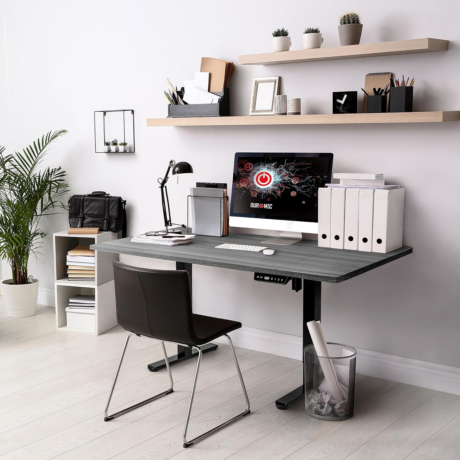 Ein Schreibtisch mit Computer, Pflanze, Büchern und einem schwarzen Stuhl.