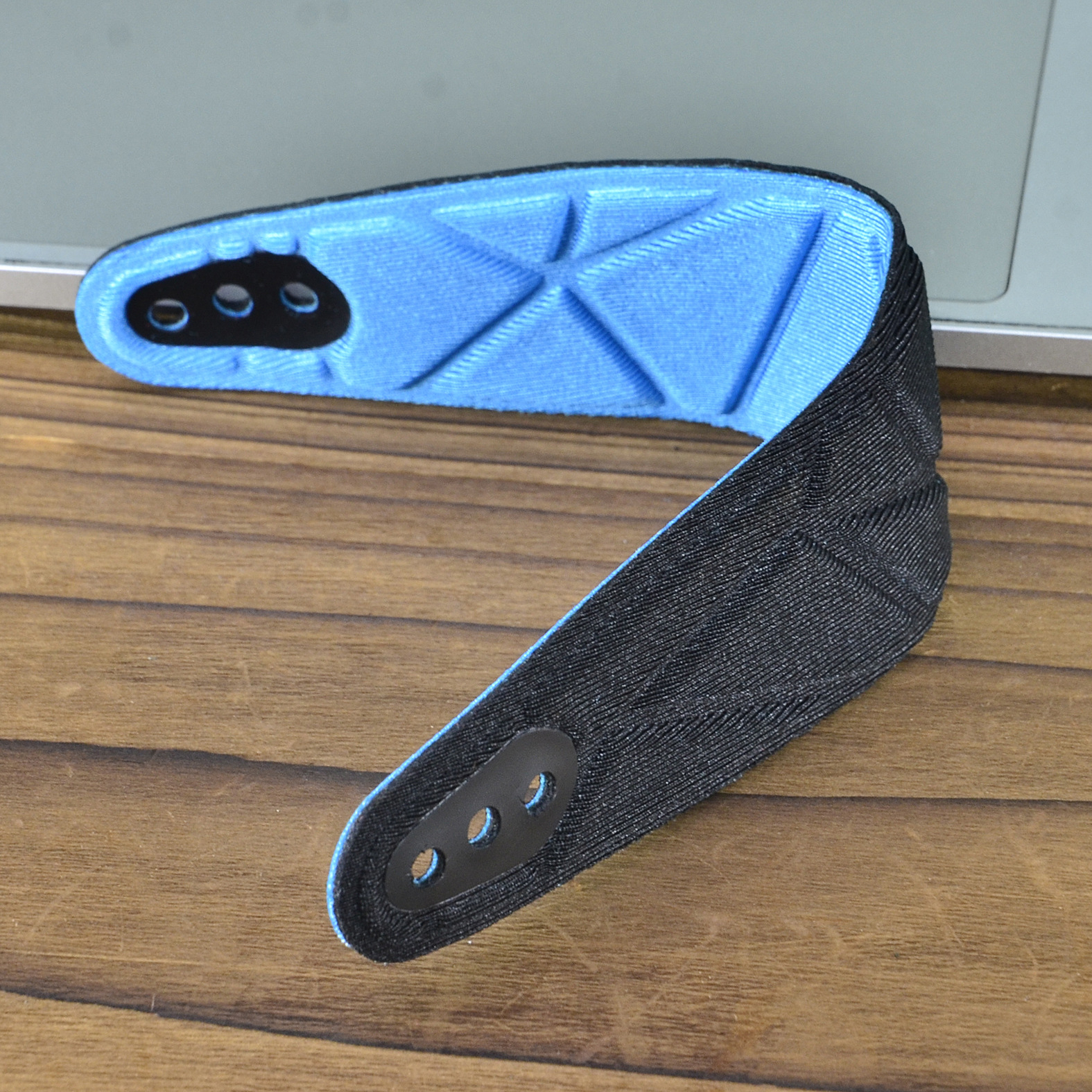 Zwart en blauw apparaat, mogelijk een wearable, op een houten oppervlak. Ziet eruit als een bandje.