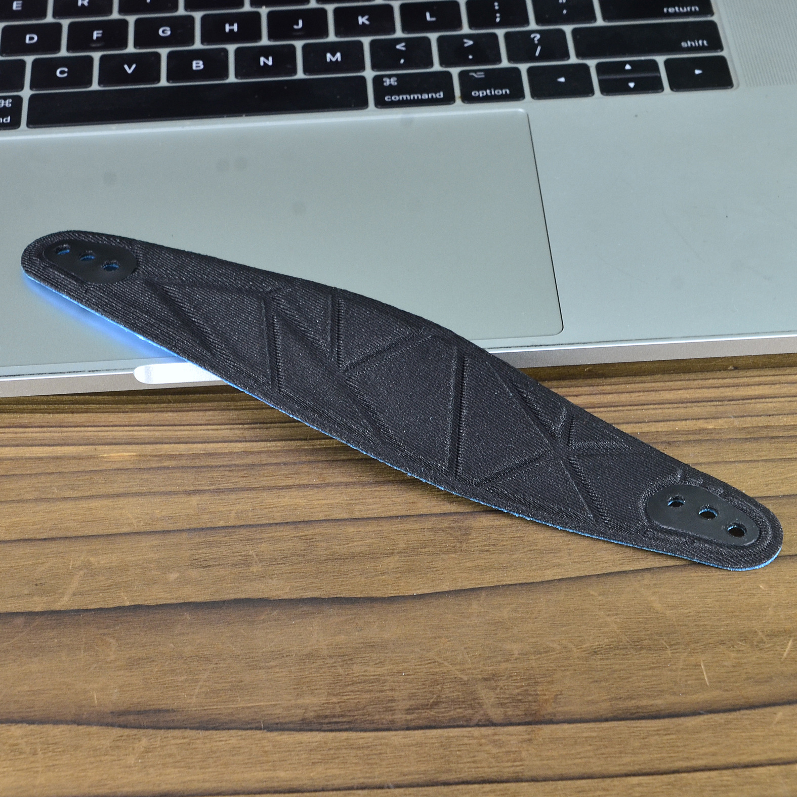 Zwart 3D-geprint object op een houten tafel met een laptop op de achtergrond.