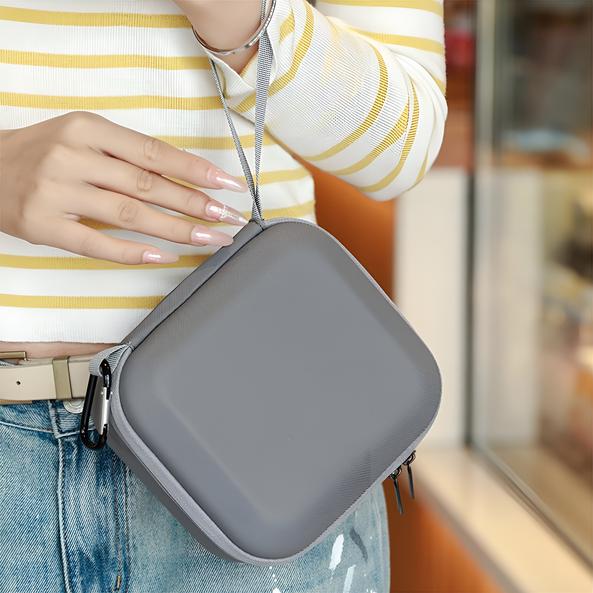 Eine Frau hält eine graue quadratische Tasche mit einem Gurt.