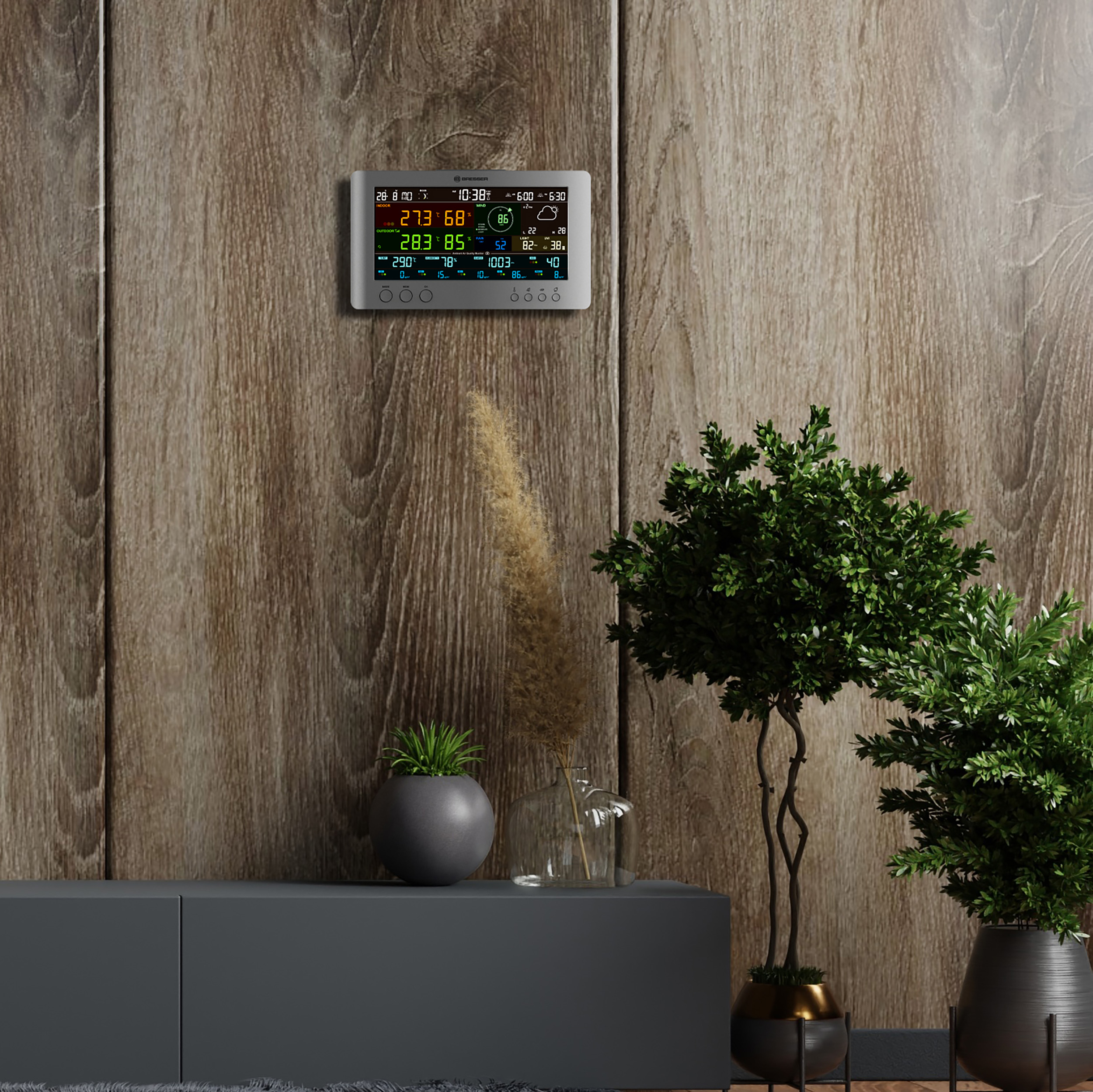 Wetterstation an einer Holzwand, mit Pflanzen auf einem grauen Schrank darunter.