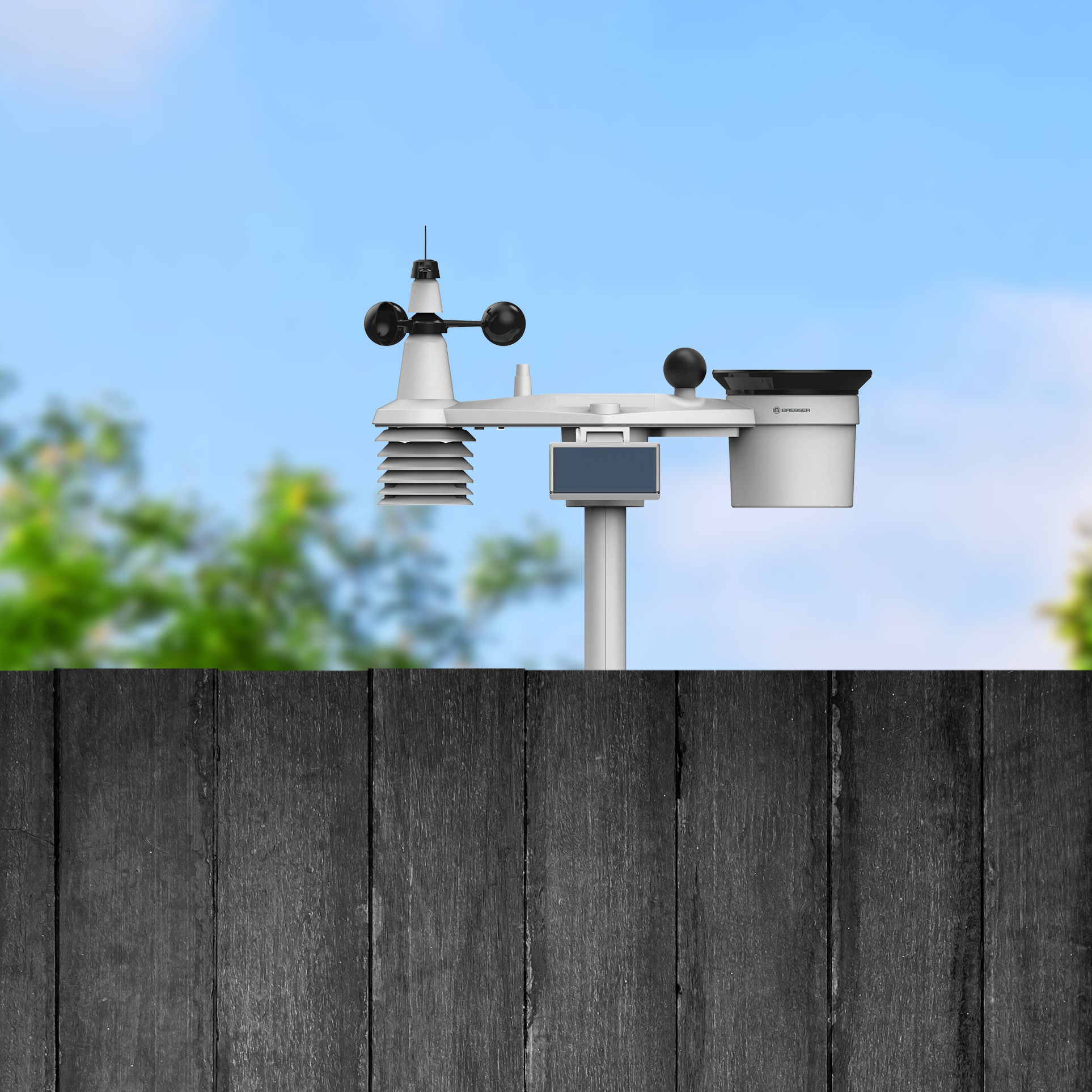 Eine weiße Wetterstation auf einem Pfahl, im Vordergrund ein Holzzaun.