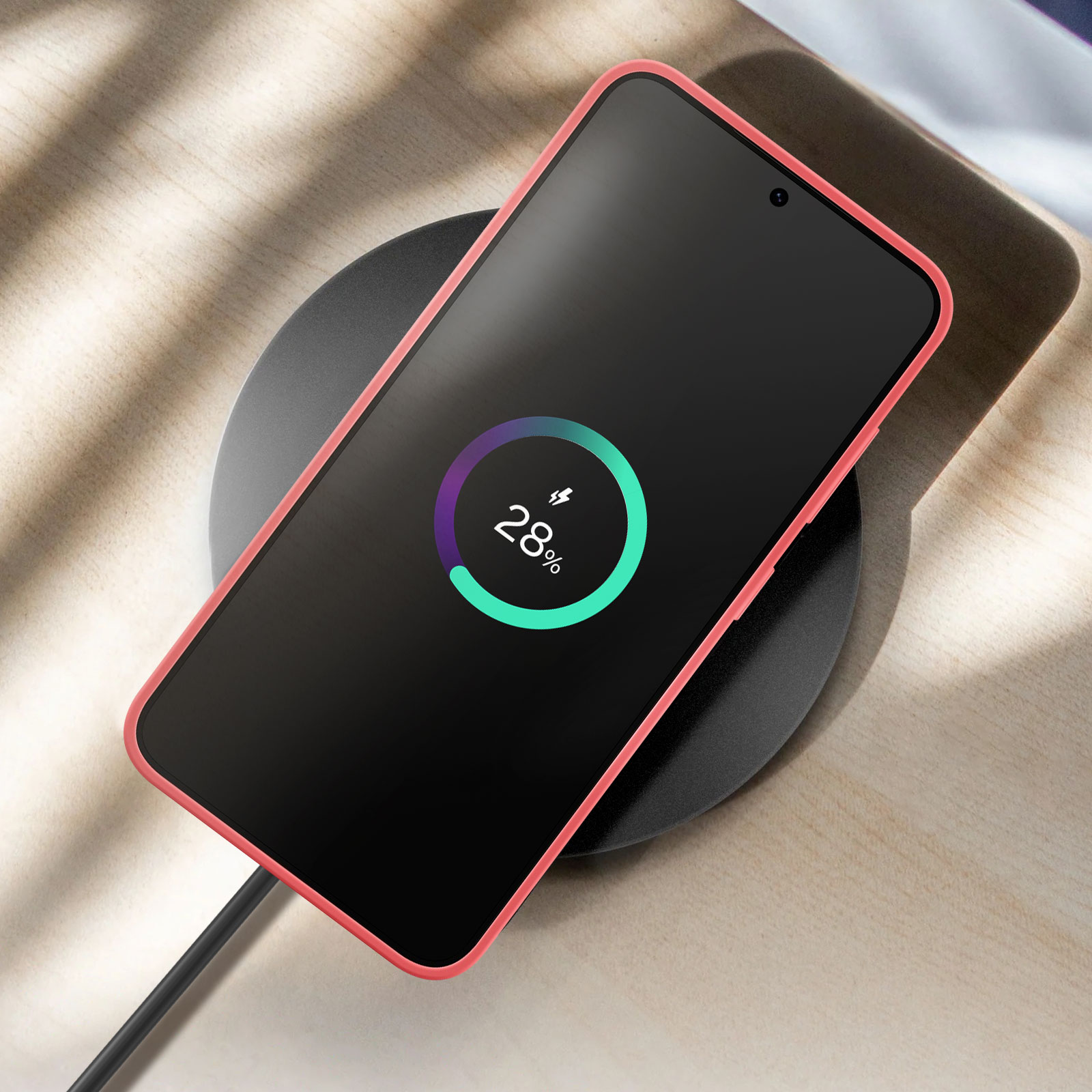 Smartfon ładujący się bezprzewodowo na czarnej podkładce ładującej z różowym etui na drewnianej powierzchni.