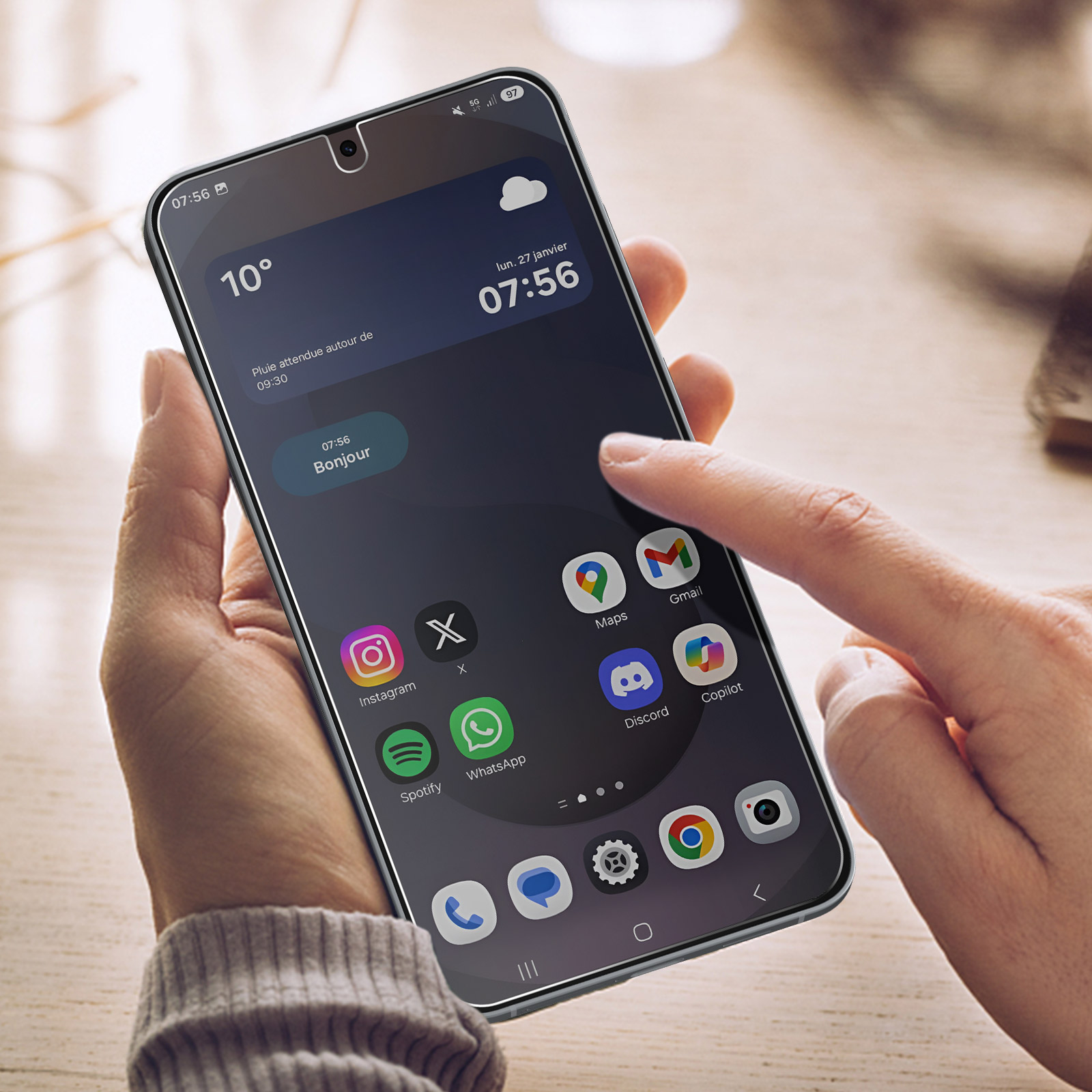 Une personne tenant un smartphone affichant l'heure et la météo, ainsi que des icônes d'applications sur l'écran d'accueil.