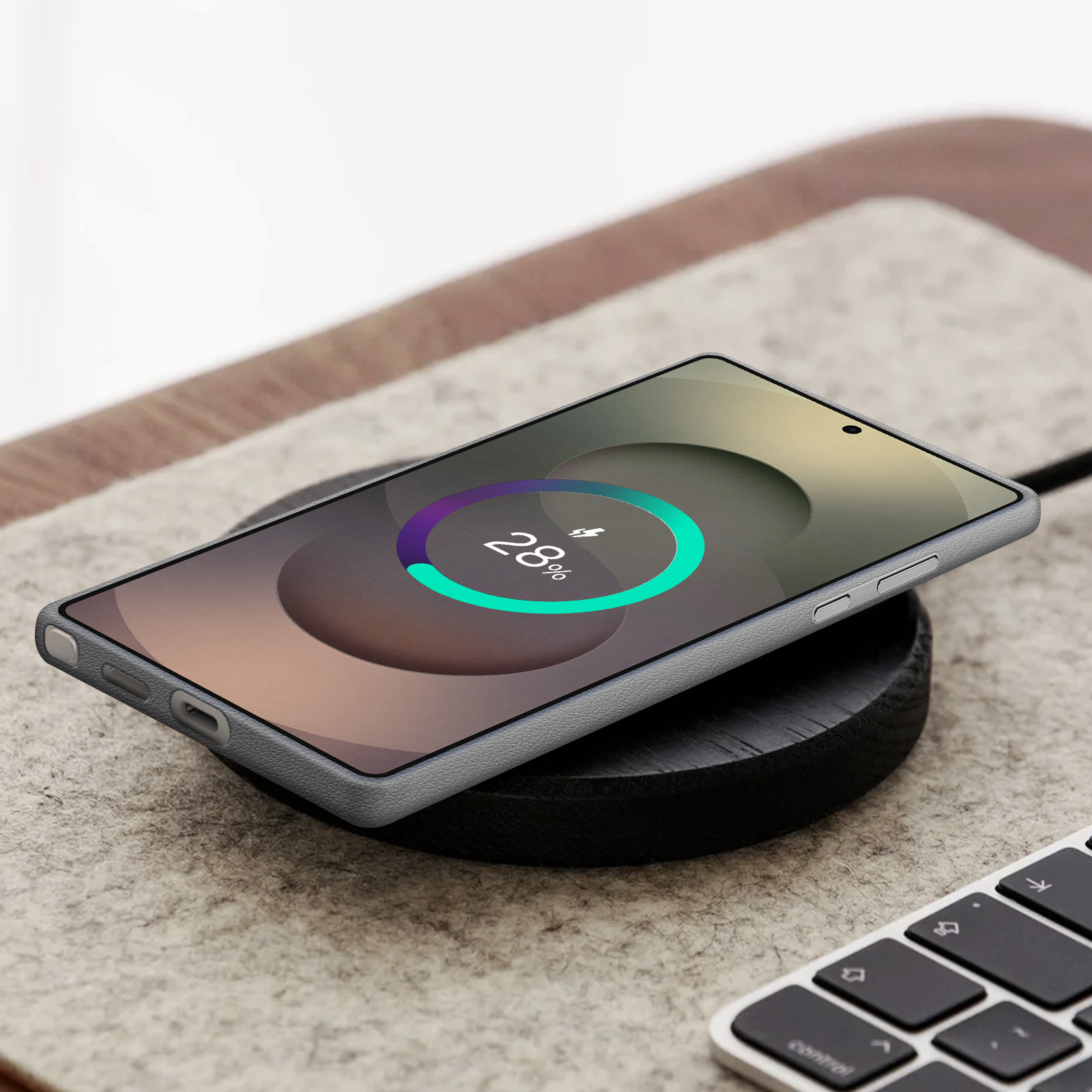 Un téléphone gris se chargeant sans fil sur une base en bois, avec un clavier devant et un indicateur de charge.