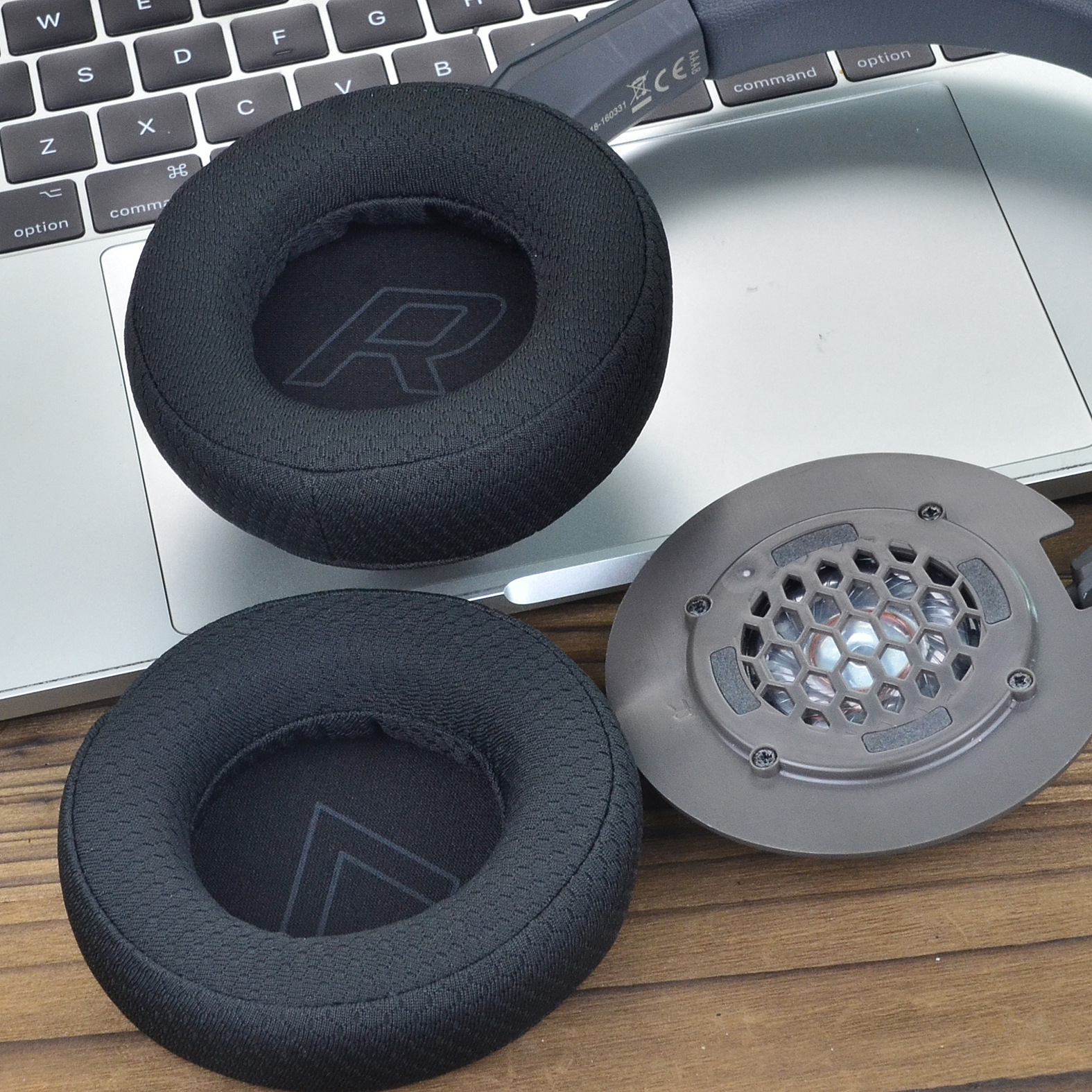 Na klawiaturze laptopa znajdują się nauszniki i elementy wewnętrzne słuchawek. Nauszniki są czarne z literą "R".