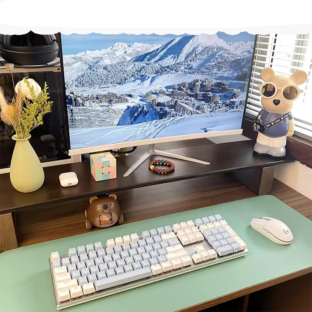 Ein Schreibtisch-Setup mit Monitor, Tastatur, Maus und dekorativen Gegenständen. Der Hintergrund zeigt eine schneebedeckte Berglandschaft.