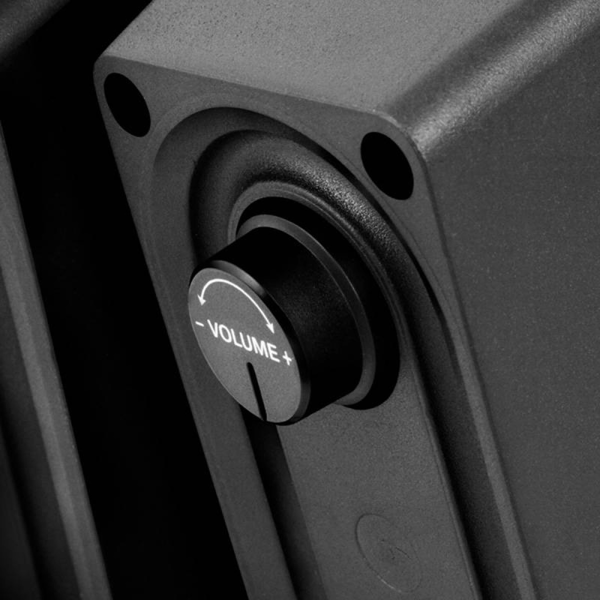 Primo piano di una manopola del volume nera su un altoparlante grigio scuro. Testo volume + bianco è visibile.