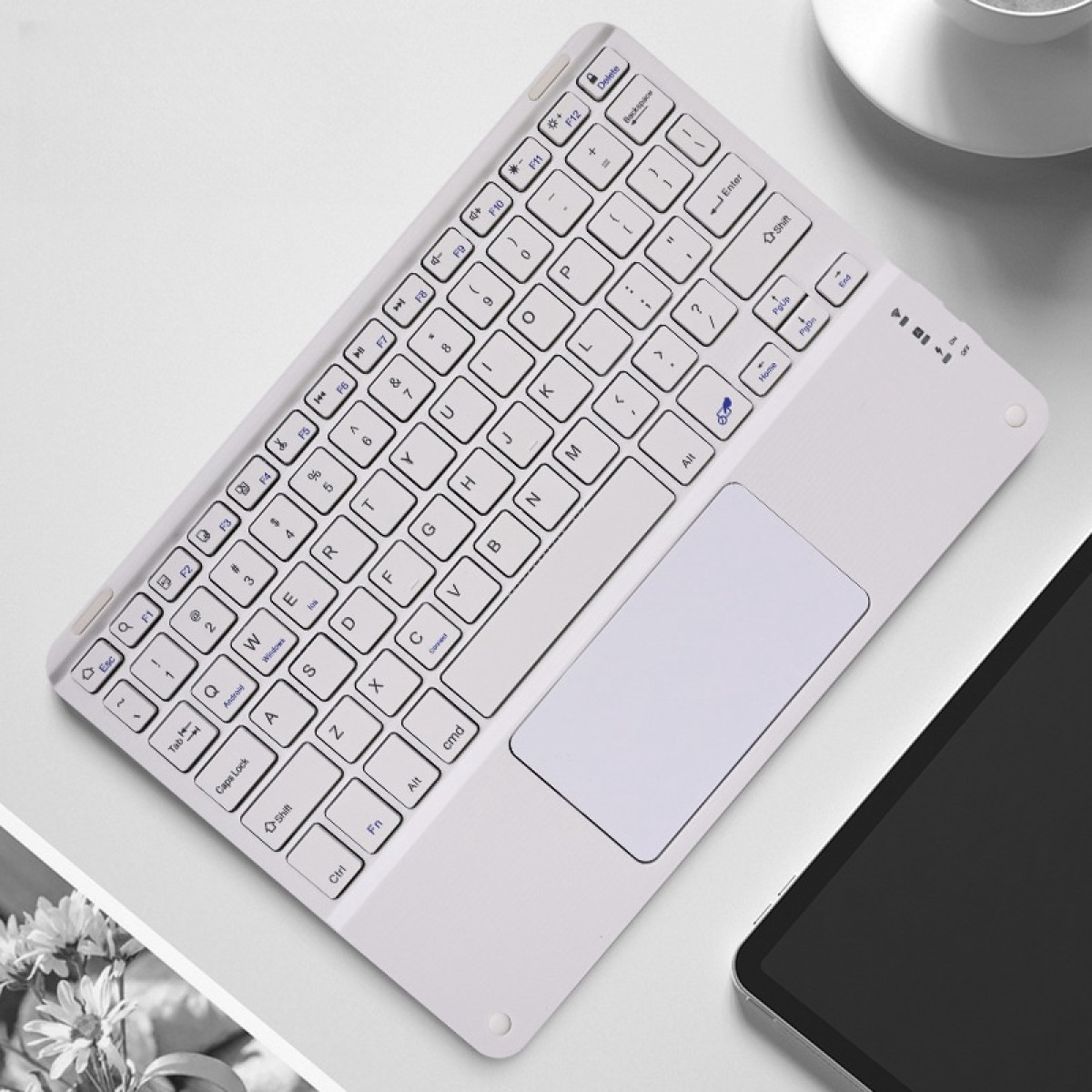 Tastiera bianca con touchpad, su superficie bianca e tablet. Focus sulla tastiera.