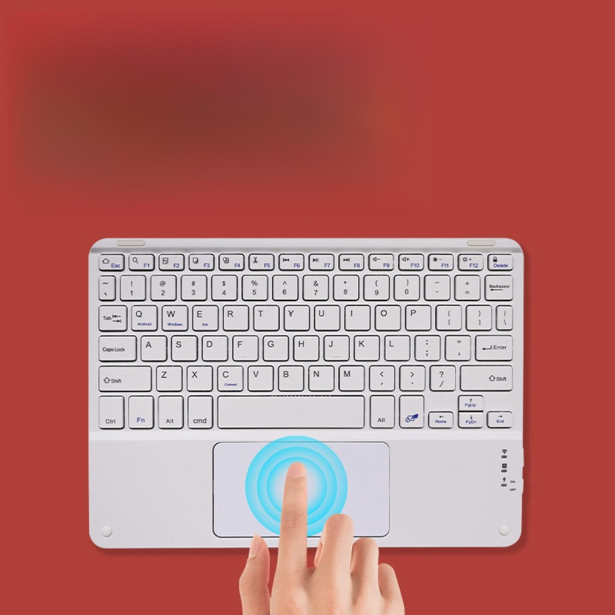 Una tastiera bianca con un trackpad su sfondo rosso. Un dito tocca il trackpad.