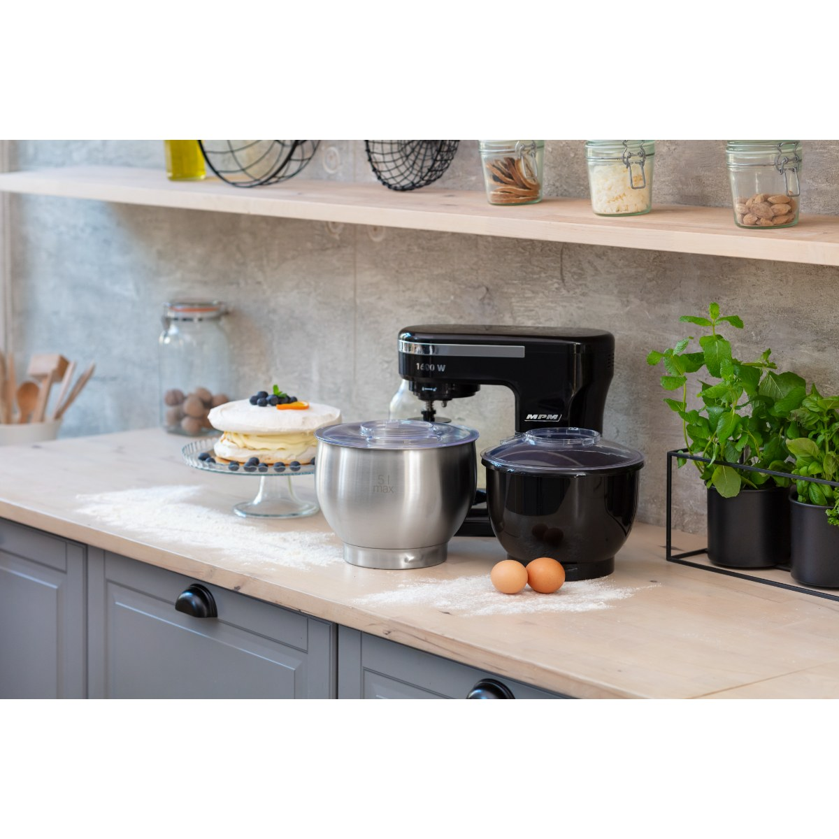 Czarny mikser stojący z miskami i jajkami. Ciasto po lewej stronie, a drewniana półka w tle.