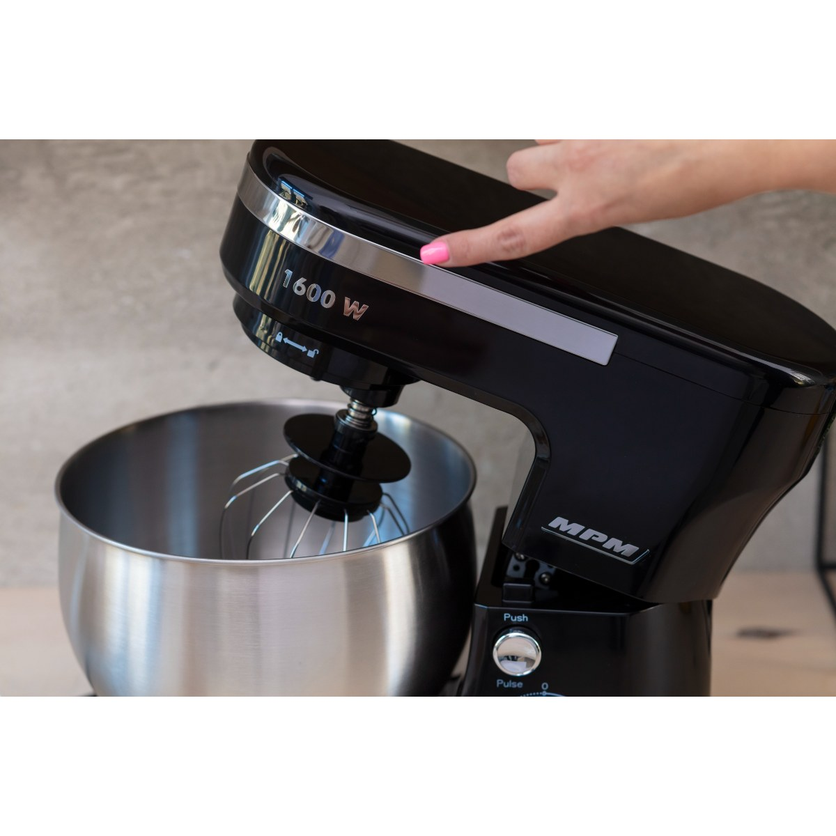 Czarny mikser ze srebrną misą. Ręka kobiety naciska przycisk.