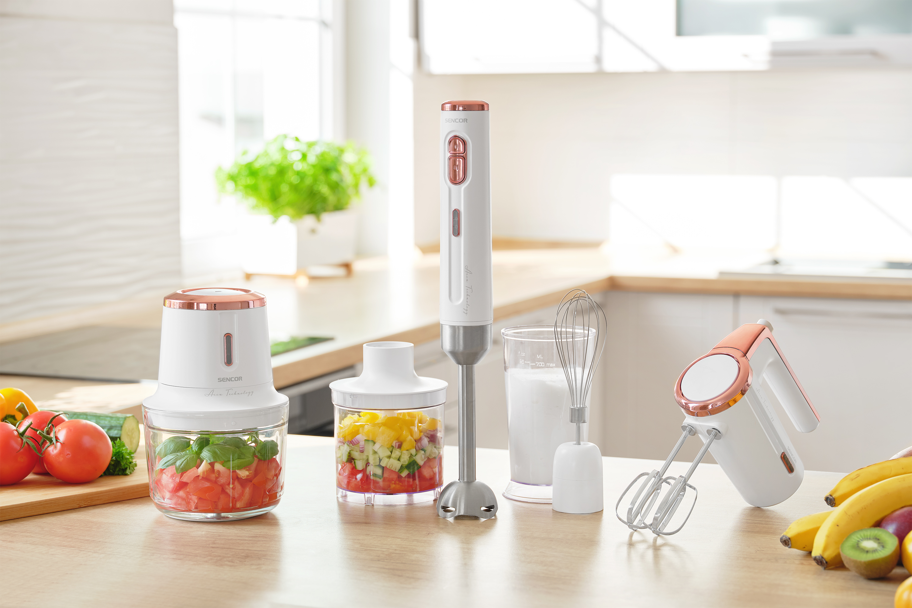 Scena di cucina con vari elettrodomestici da cucina bianchi e oro rosa su una superficie di legno con ingredienti.