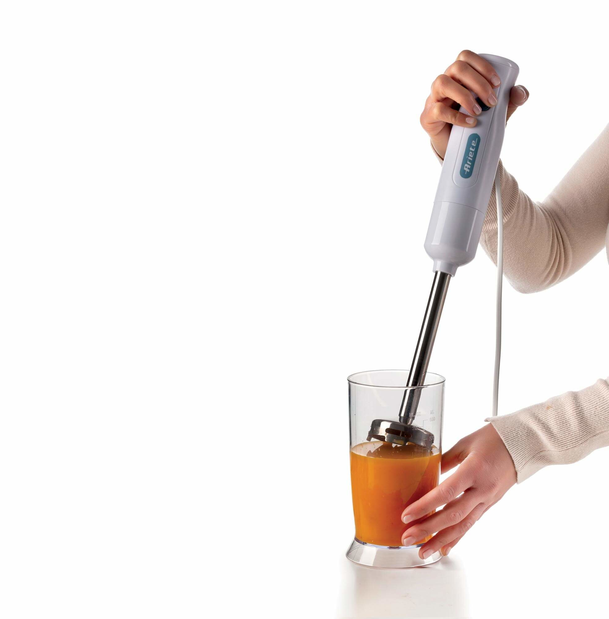 Osoba trzymająca biały blender ręczny, miksująca płyn w szklance.