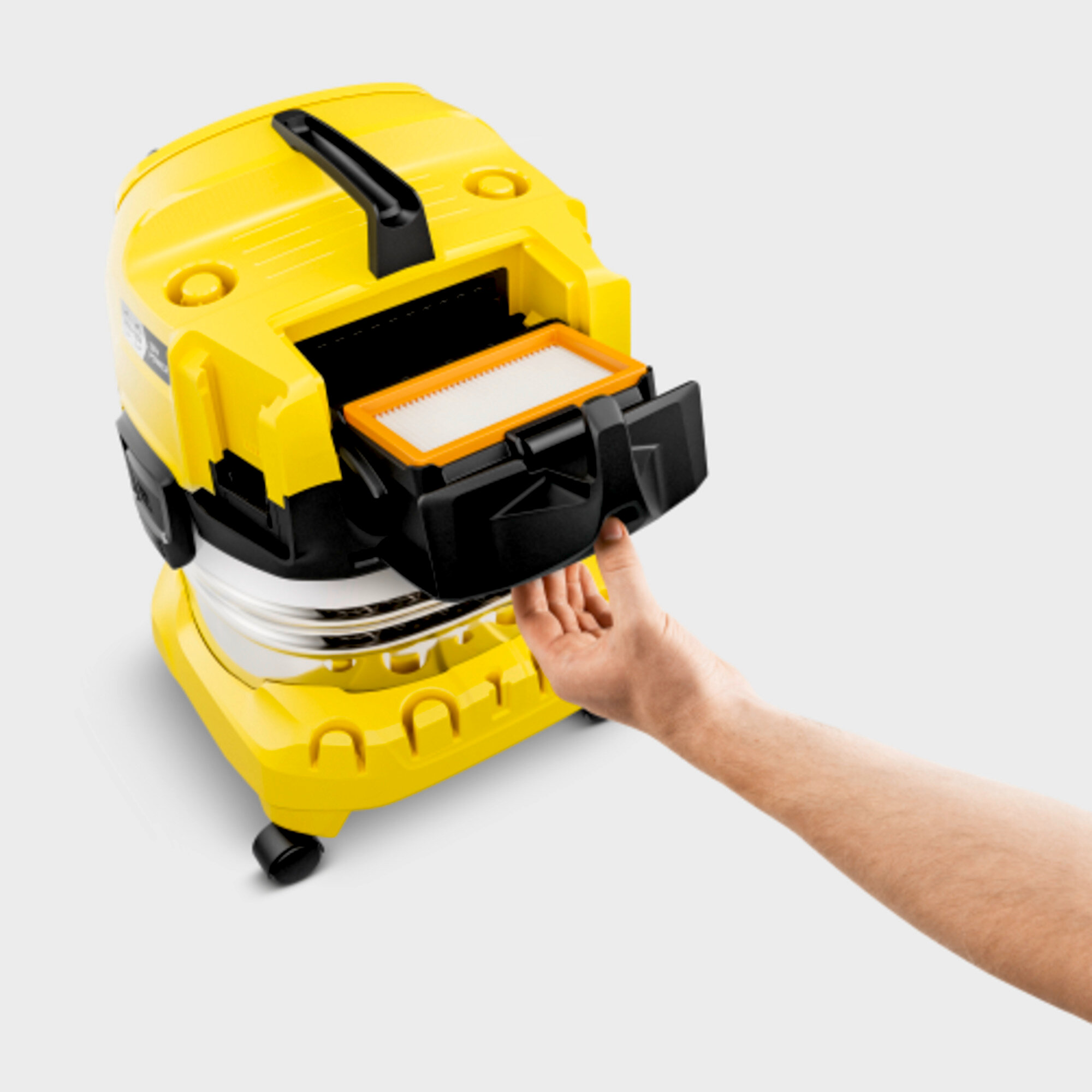 Aspirapolvere giallo con vano aperto, filtro visibile, mano dentro. Sfondo bianco.