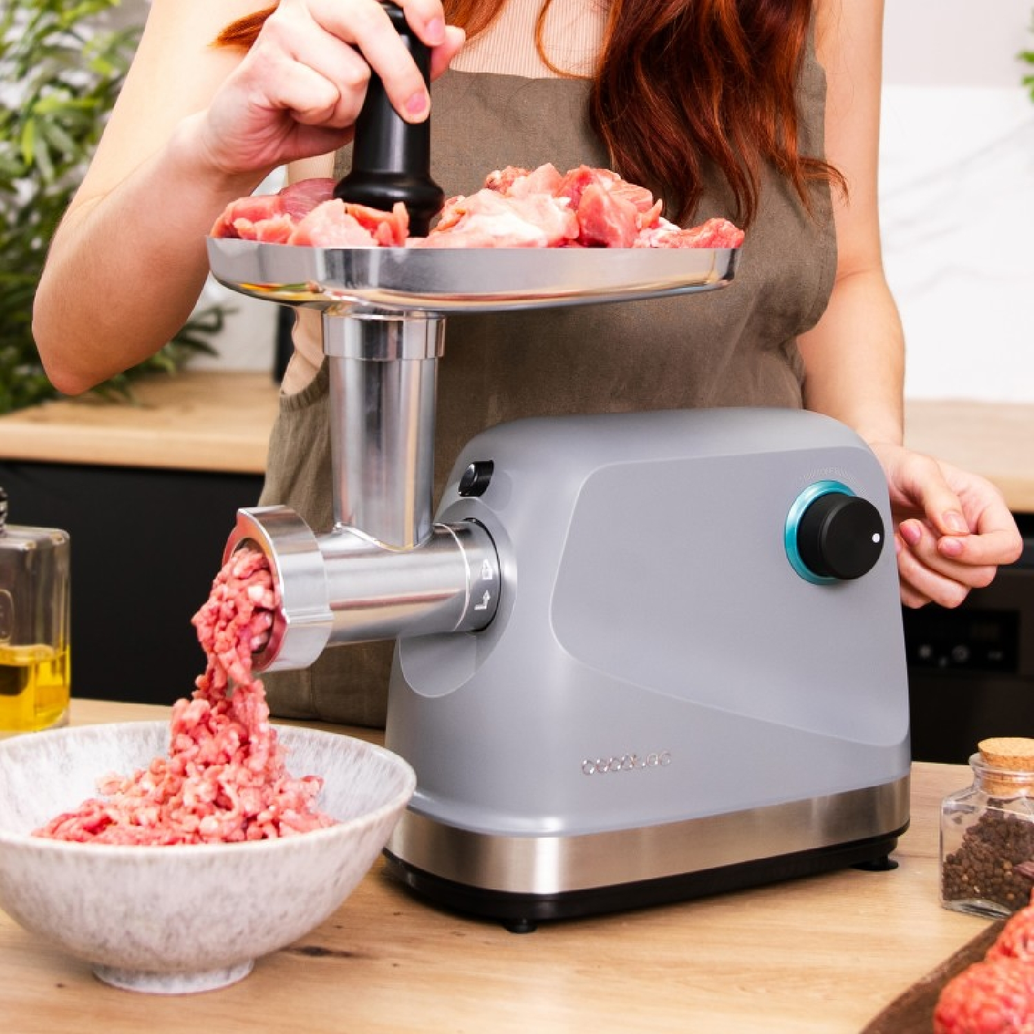 Donna che usa un tritacarne, tritando la carne in una ciotola su una superficie di legno, con ingredienti nelle vicinanze.
