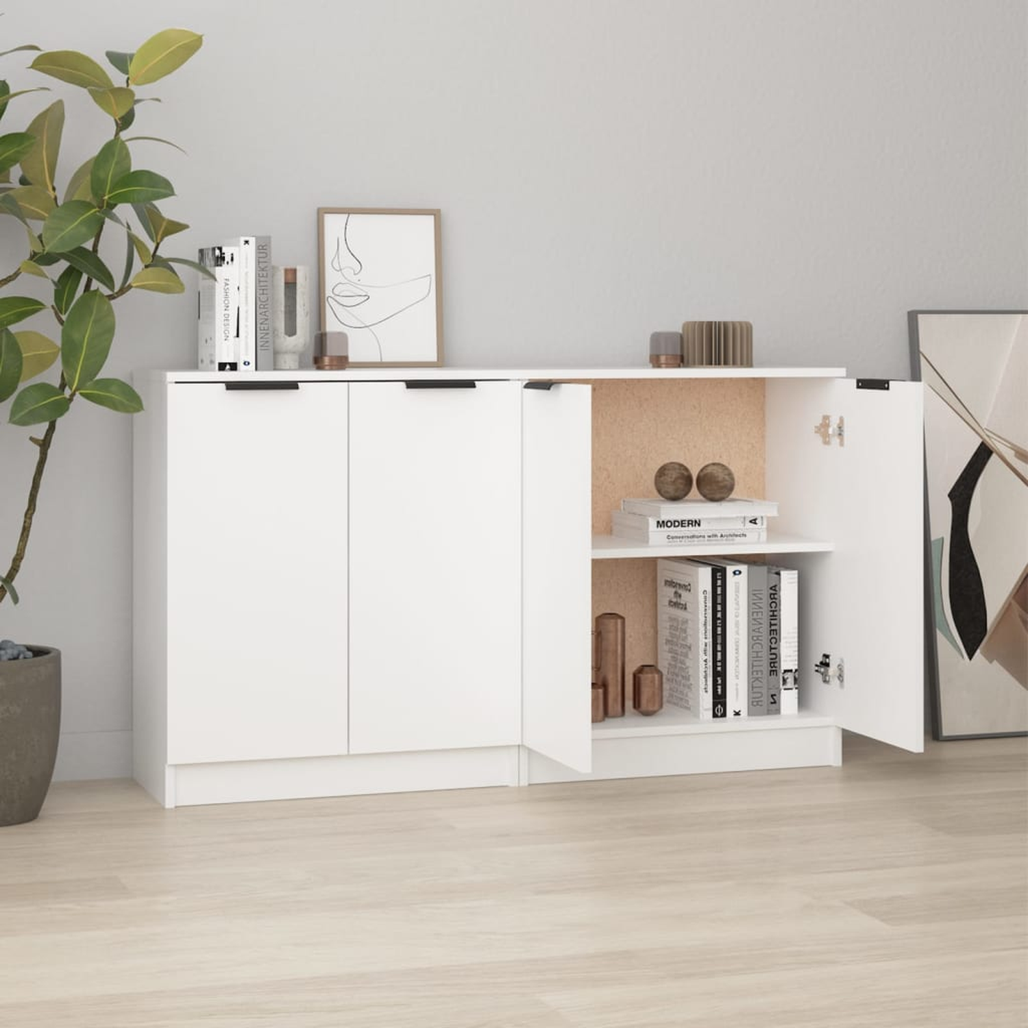 Weißer Schrank mit offenen Türen und Büchern im Inneren. Pflanze und Kunstwerk im Hintergrund.