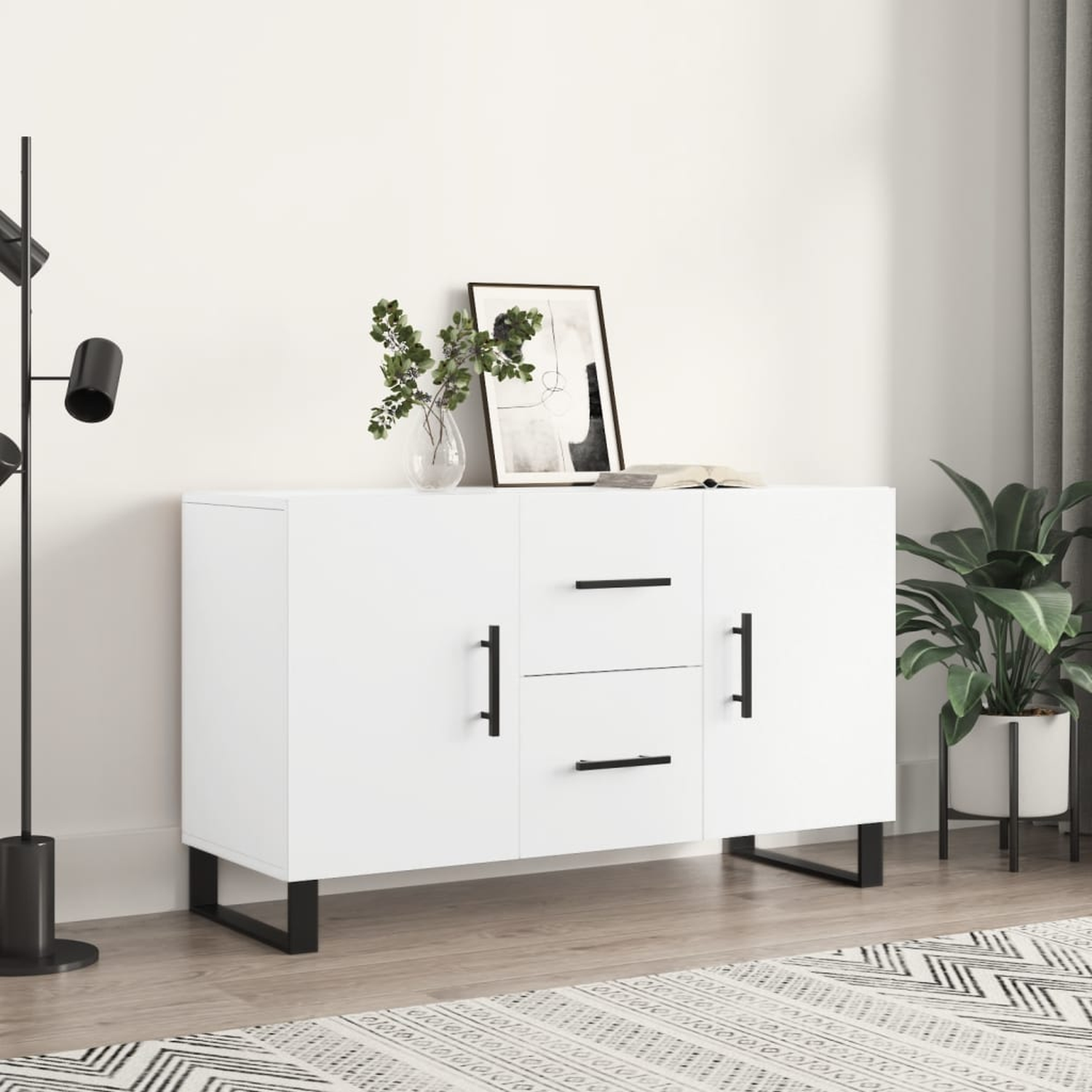 Ein weißer Schrank mit schwarzen Griffen und Beinen, mit einer Vase und einem Bild oben drauf.