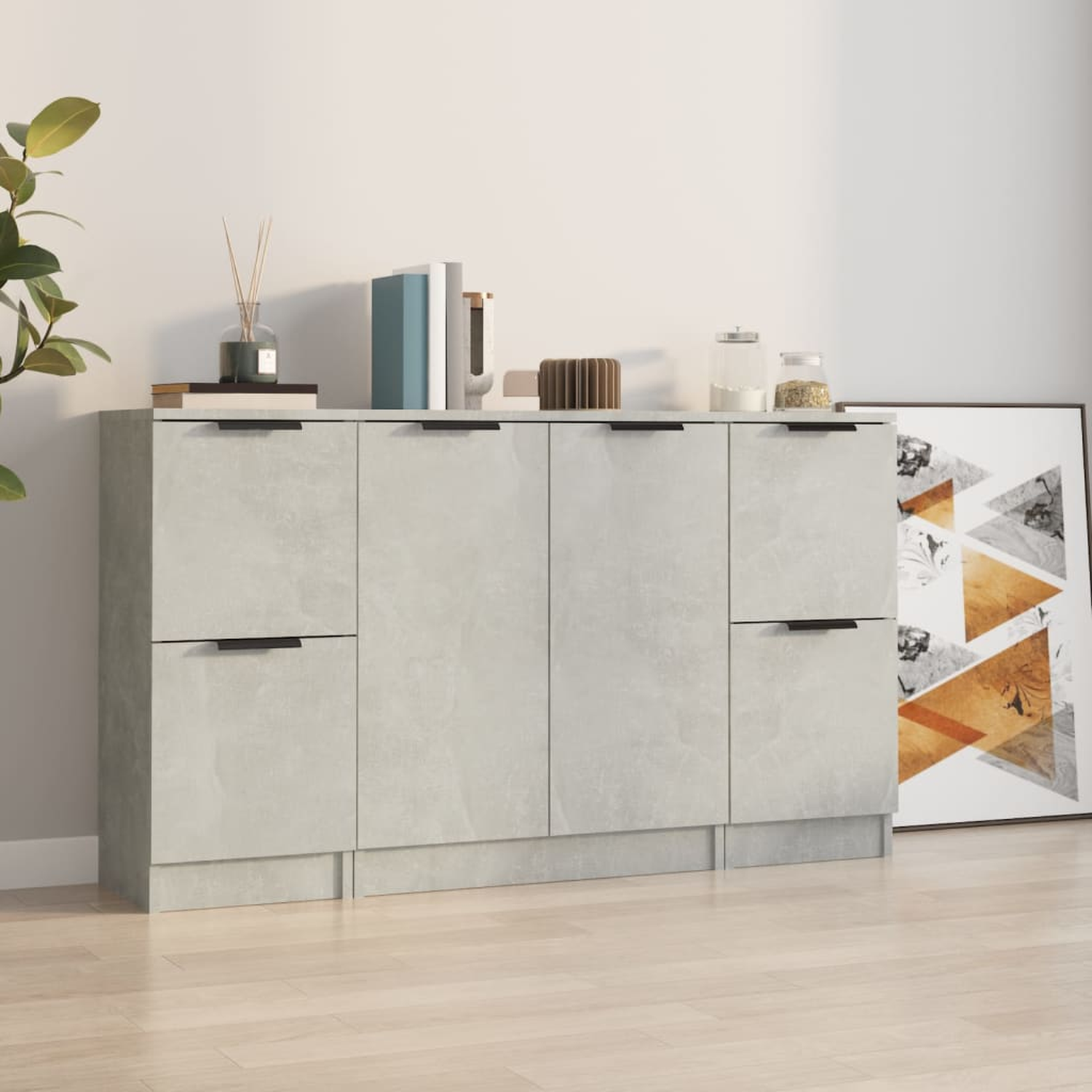 Ein hellgrauer Schrank mit vier Türen und zwei Schubladen. Er steht vor einer Wand mit Dekoration.
