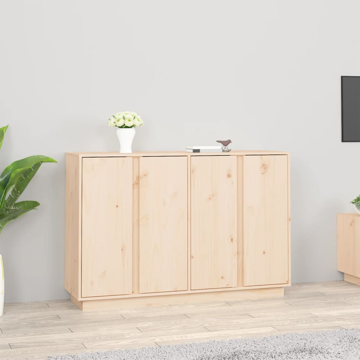 Ein helles Holzschrank mit zwei Türen. Eine weiße Vase mit Blumen und ein kleiner Dekovogel oben.