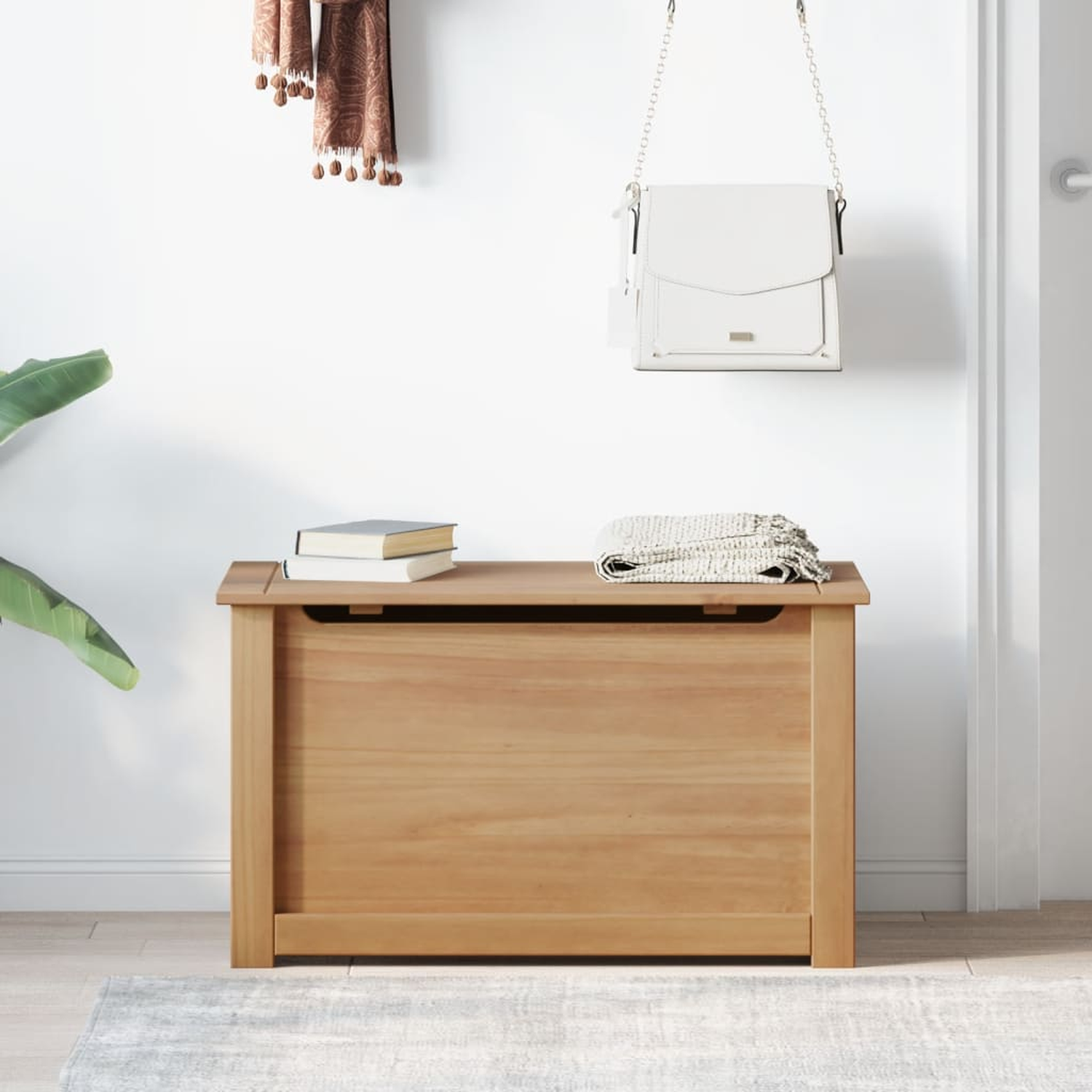 Holz-Truhe mit Büchern und Decke, weißer Hintergrund. Eine Handtasche hängt an der Wand.