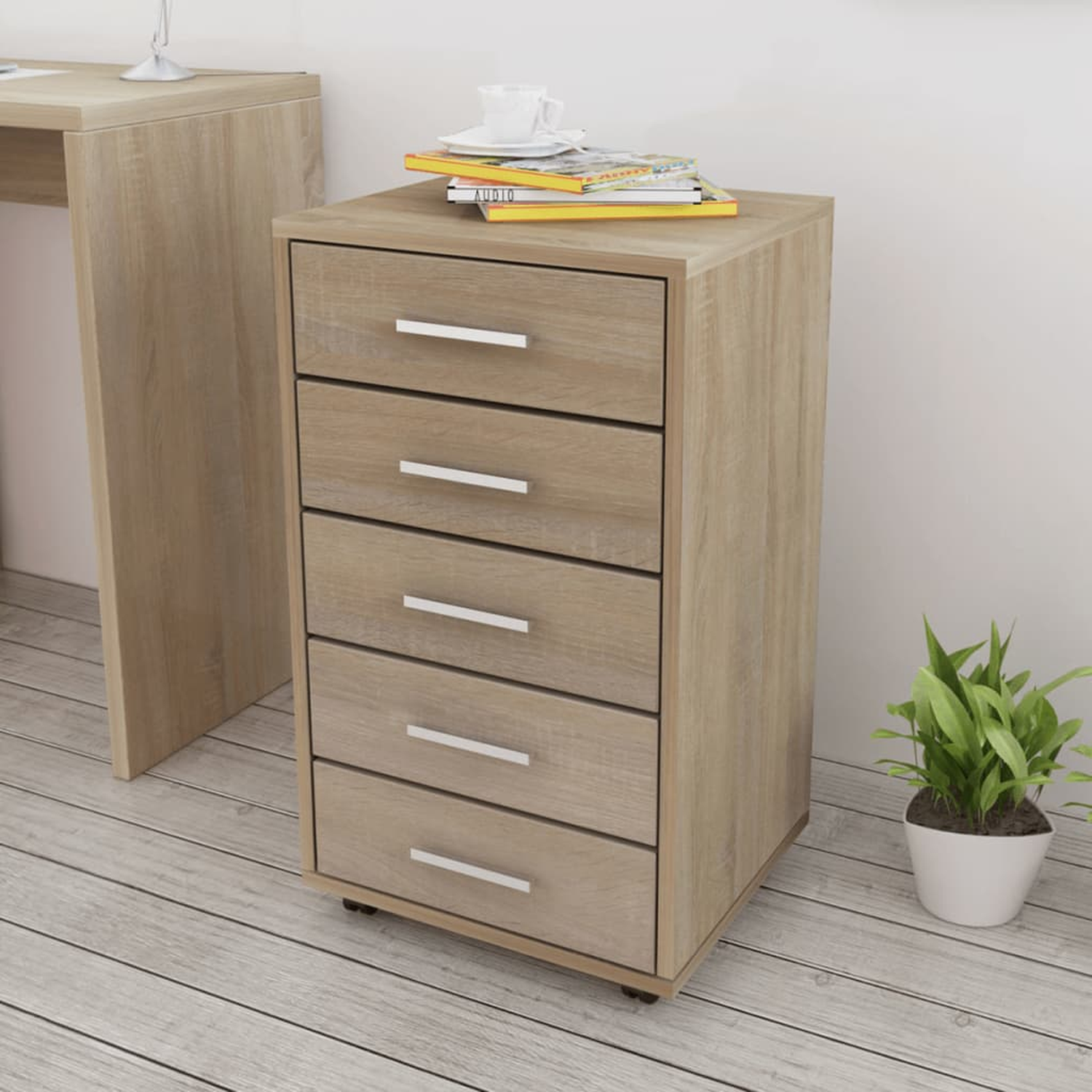 Holzschrank mit Schubladen, Büchern und einer Pflanze. Im Hintergrund ein Schreibtisch.