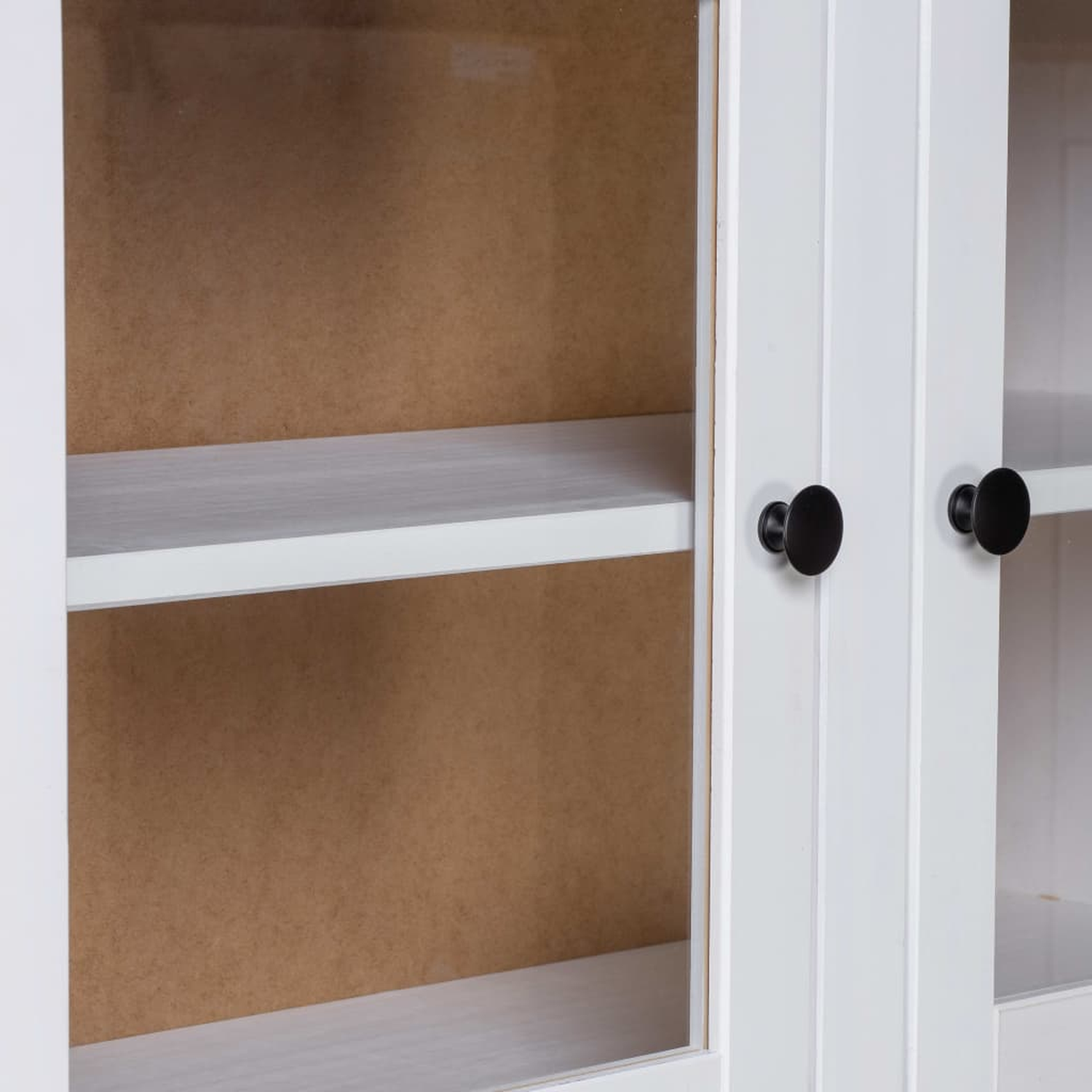 Weißer Schrank mit Glastüren, schwarzen Griffen. Innere Regale sichtbar. Braune Rückwand.