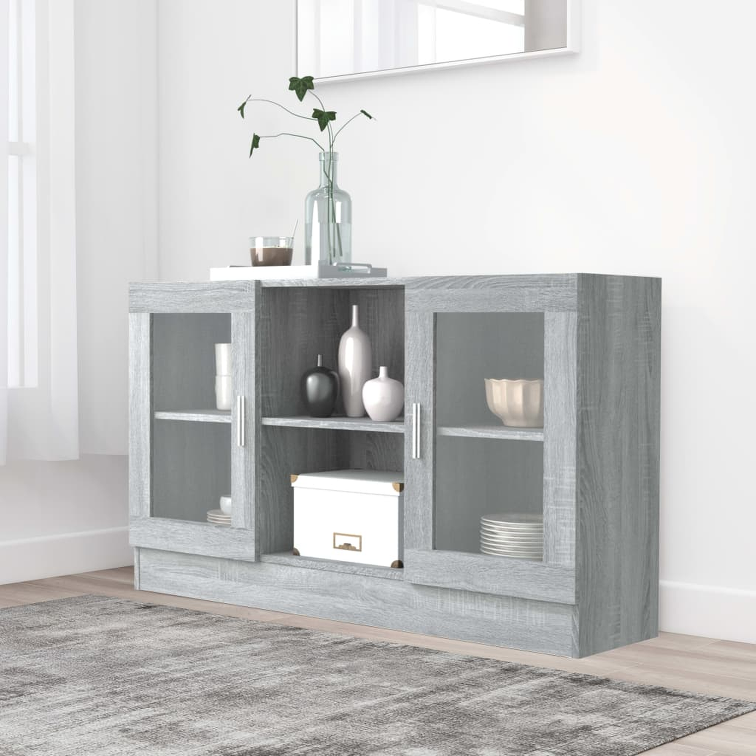 Ein grauer Schrank mit Glastüren, Regalen und Dekorationsartikeln oben. Darunter ein Teppich.
