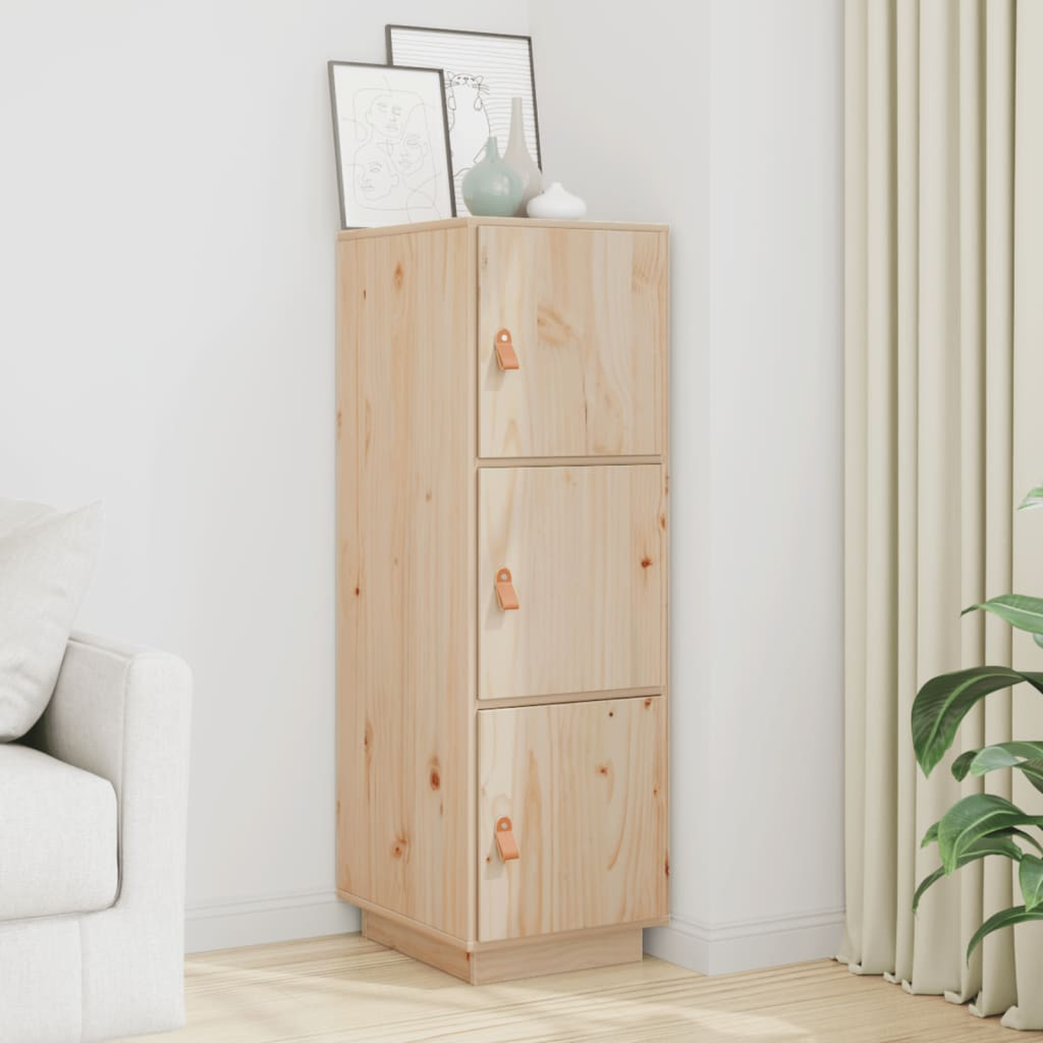 Hoher Schrank aus hellem Holz mit drei Türen, Ledergriffen und gerahmter Kunst oben. Weiße Wand.