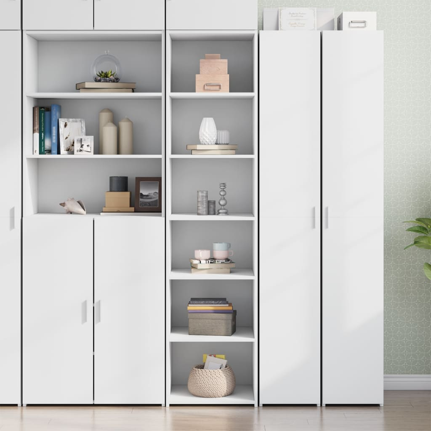 Ein weißer Schrank mit Regalen zeigt Bücher, Deko und Boxen. Geschlossene Türen sind unten. Der Hintergrund ist eine Wand.