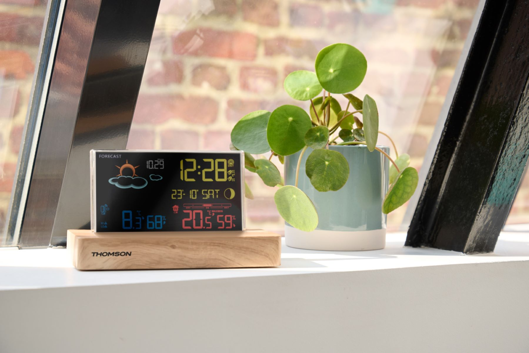 Stacja pogodowa Thomson na drewnianym stojaku, wyświetlająca czas, pogodę i temperaturę.