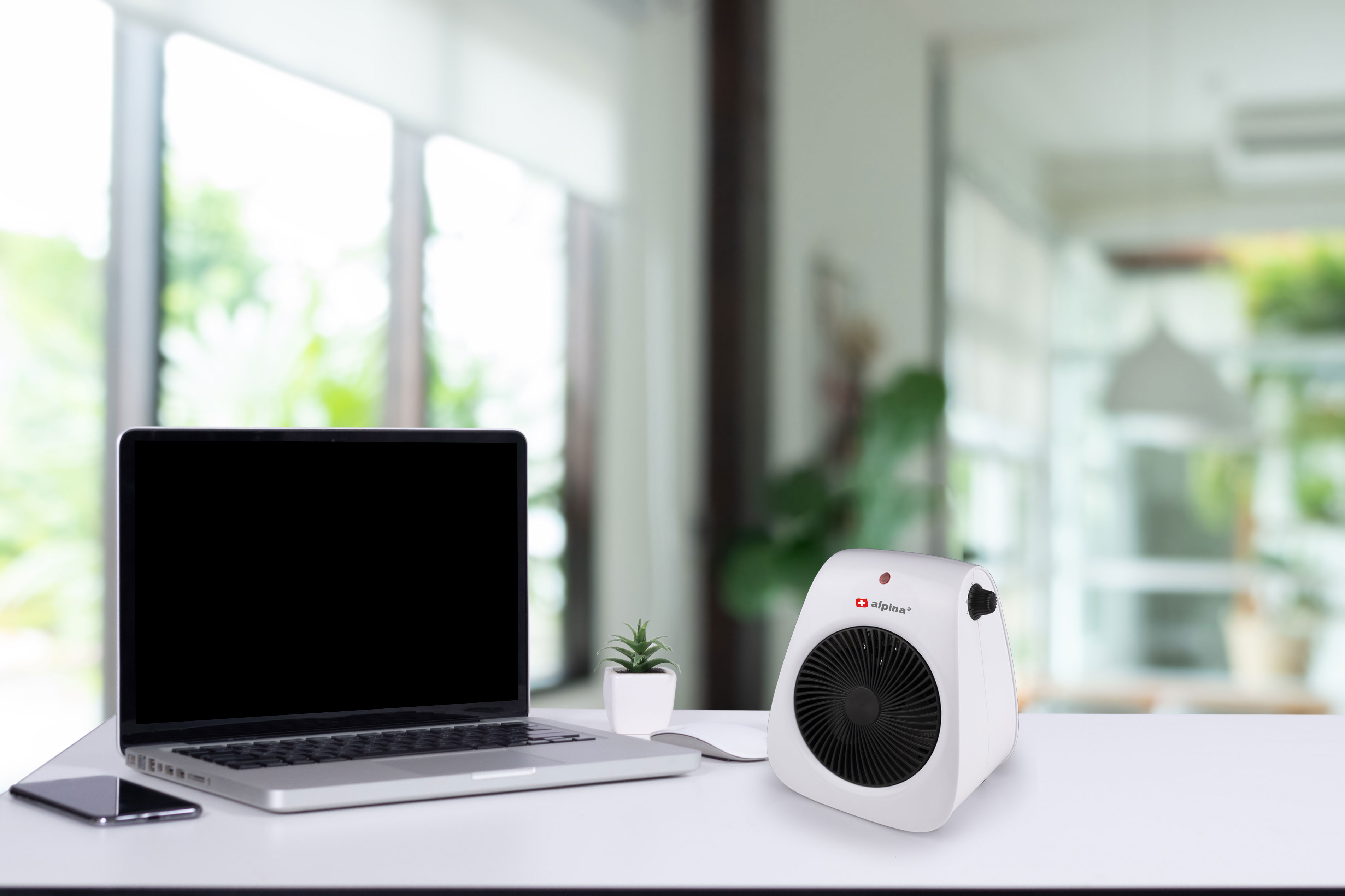A laptop, heater, and a phone on a white desk, with a window in the background.