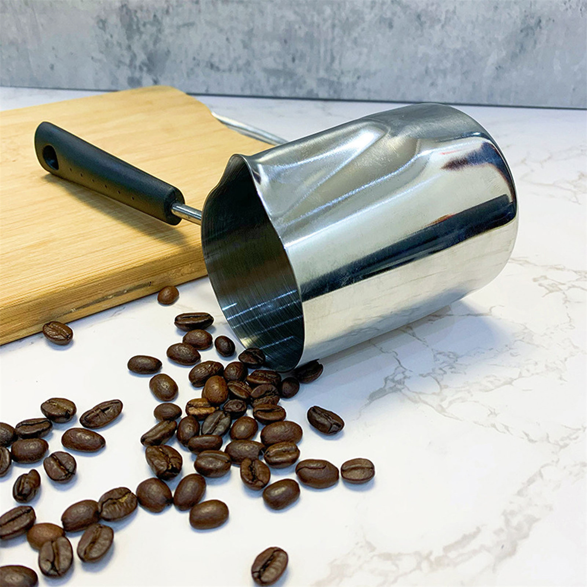 Glänzender Metallkrug mit Kaffeebohnen, die auf einer weißen Oberfläche verstreut sind.