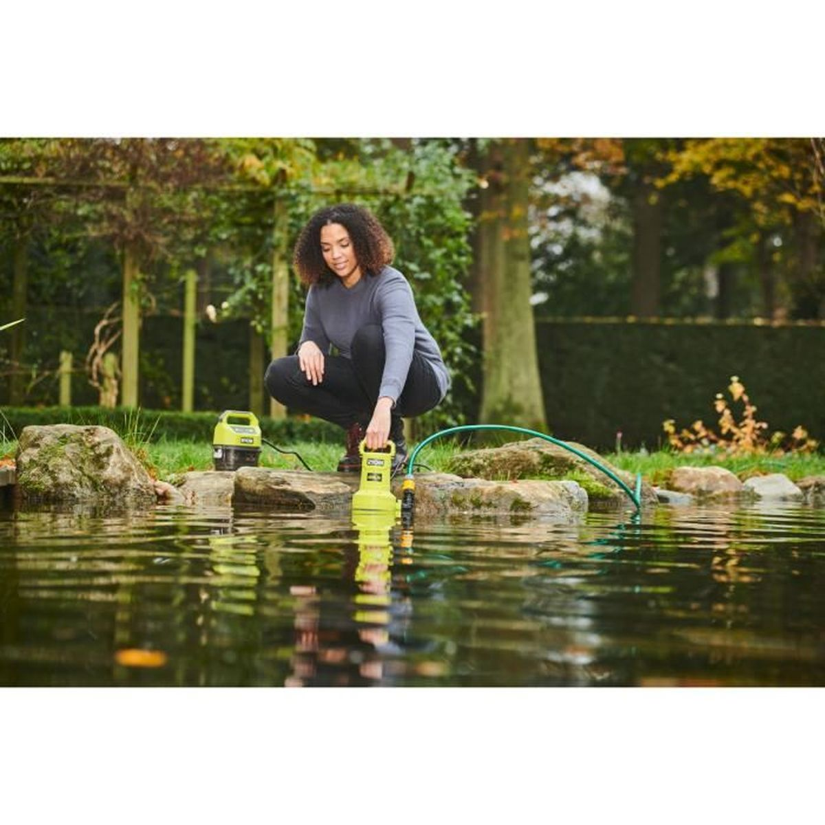 Femme agenouillée près d'un étang avec une pompe. La pompe est connectée à un tuyau.