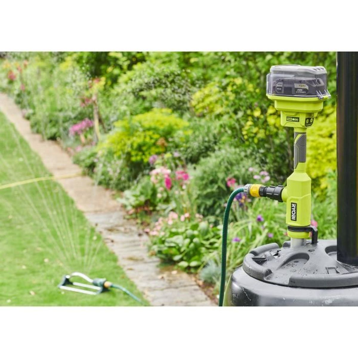 Grünes und schwarzes Bewässerungssystem in einem Garten. Ein Schlauch und ein Sprinkler sind ebenfalls sichtbar.