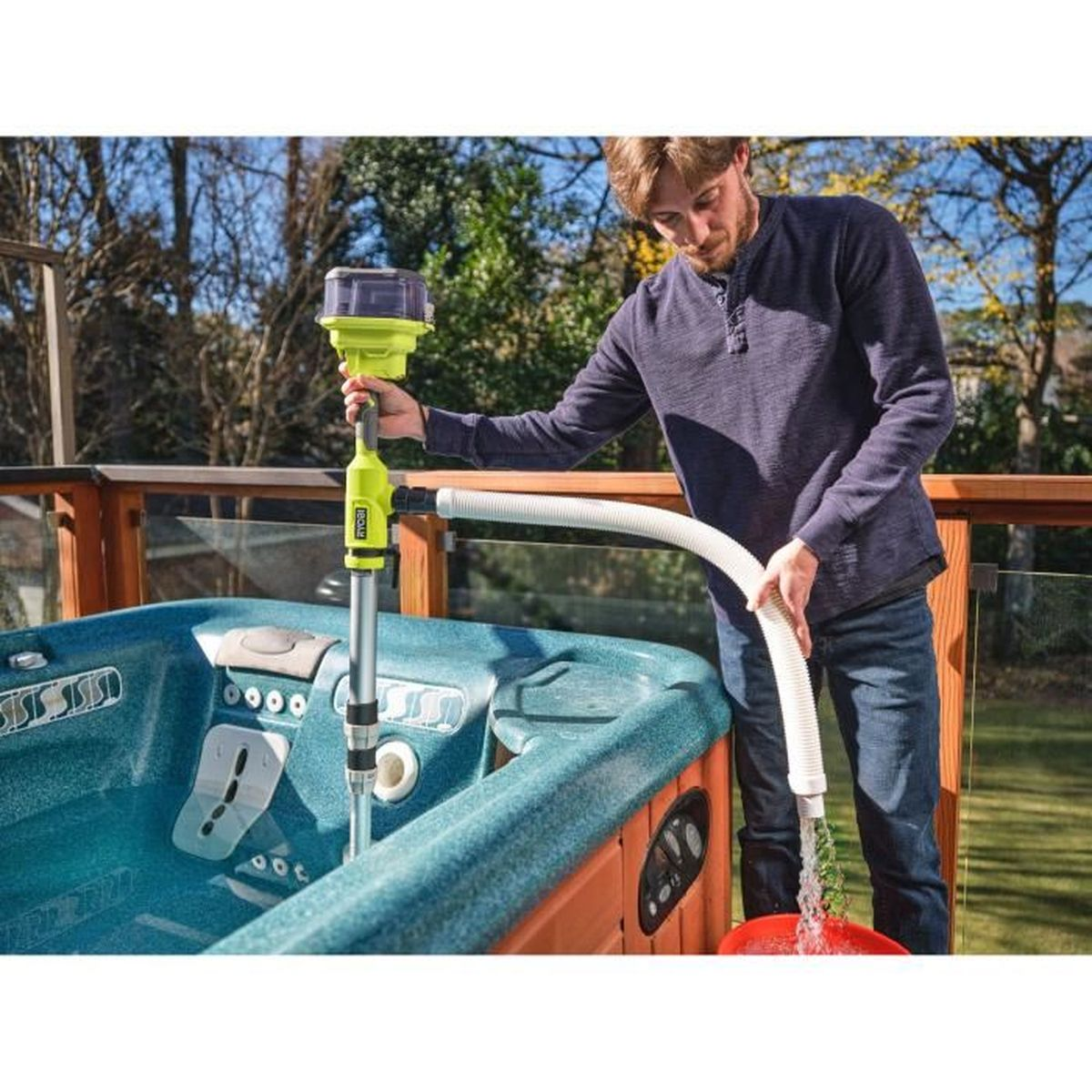 Mann pumpt Wasser aus einem Whirlpool mit einer tragbaren Pumpe und einem Schlauch, draußen auf einer Terrasse.