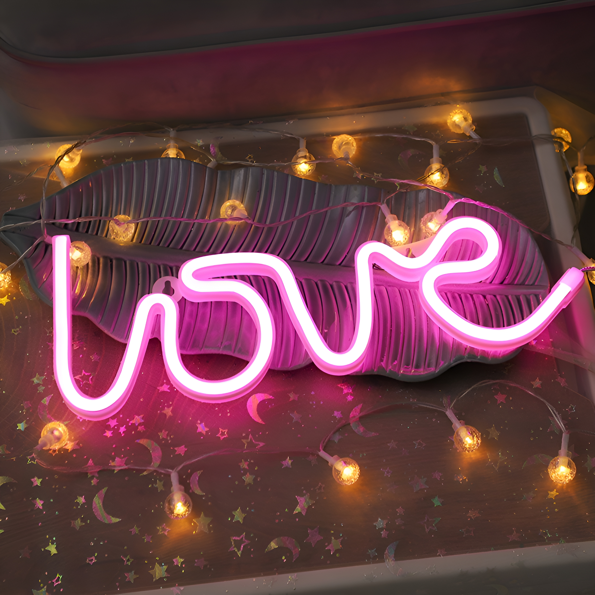 Ein neonpinkes "Love"-Schild auf einem bananenblattförmigen Tablett, mit Lichterketten.