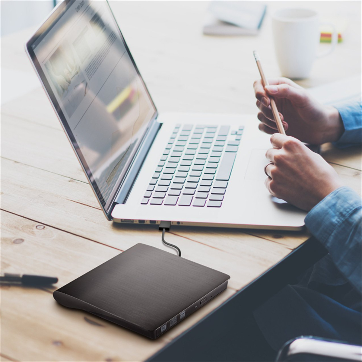 Ein Laptop, der mit einem schwarzen externen DVD-Laufwerk verbunden ist. Hände arbeiten am Laptop.