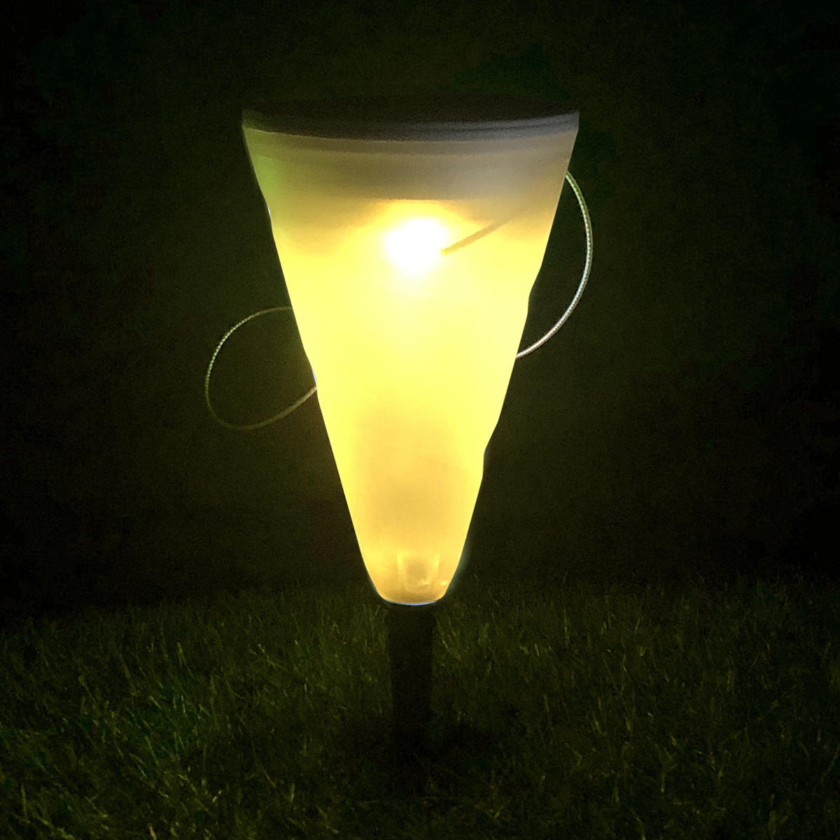 Ein leuchtendes, kegelförmiges Solarlicht im Gras bei Nacht.