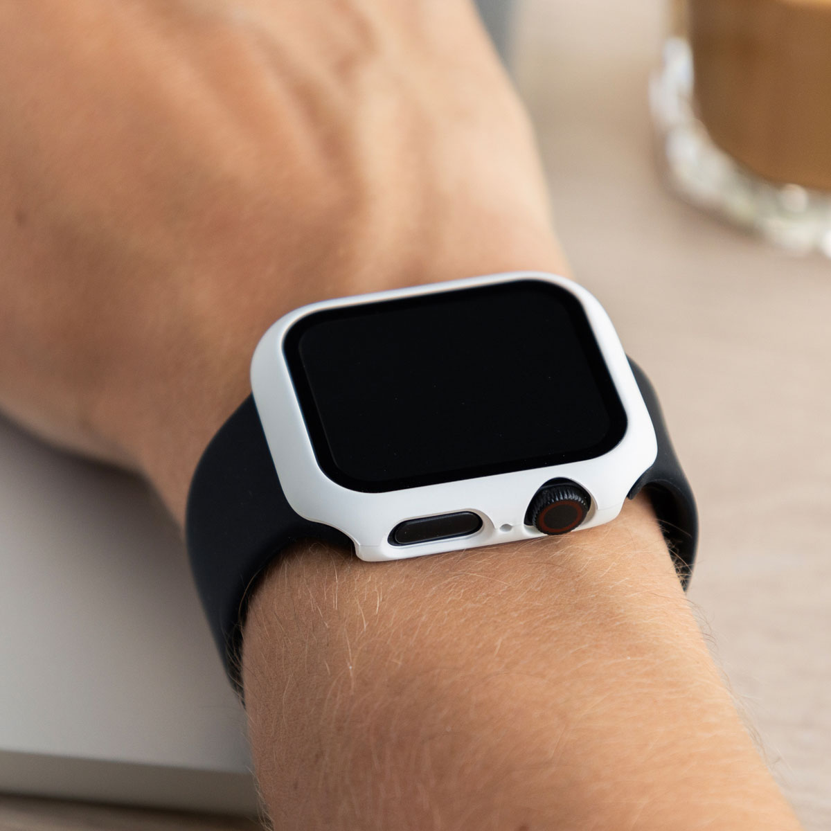 Wrist with watch, black band, white case. Background is blurred.